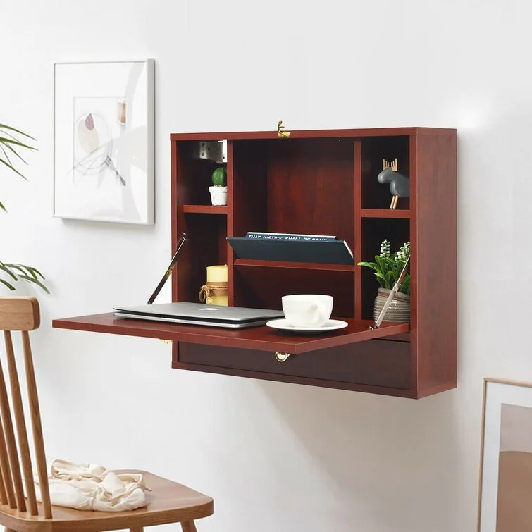 A dark wood wall-mounted fold-down desk is open, displaying internal shelves with small decor items, a laptop, and a white teacup.