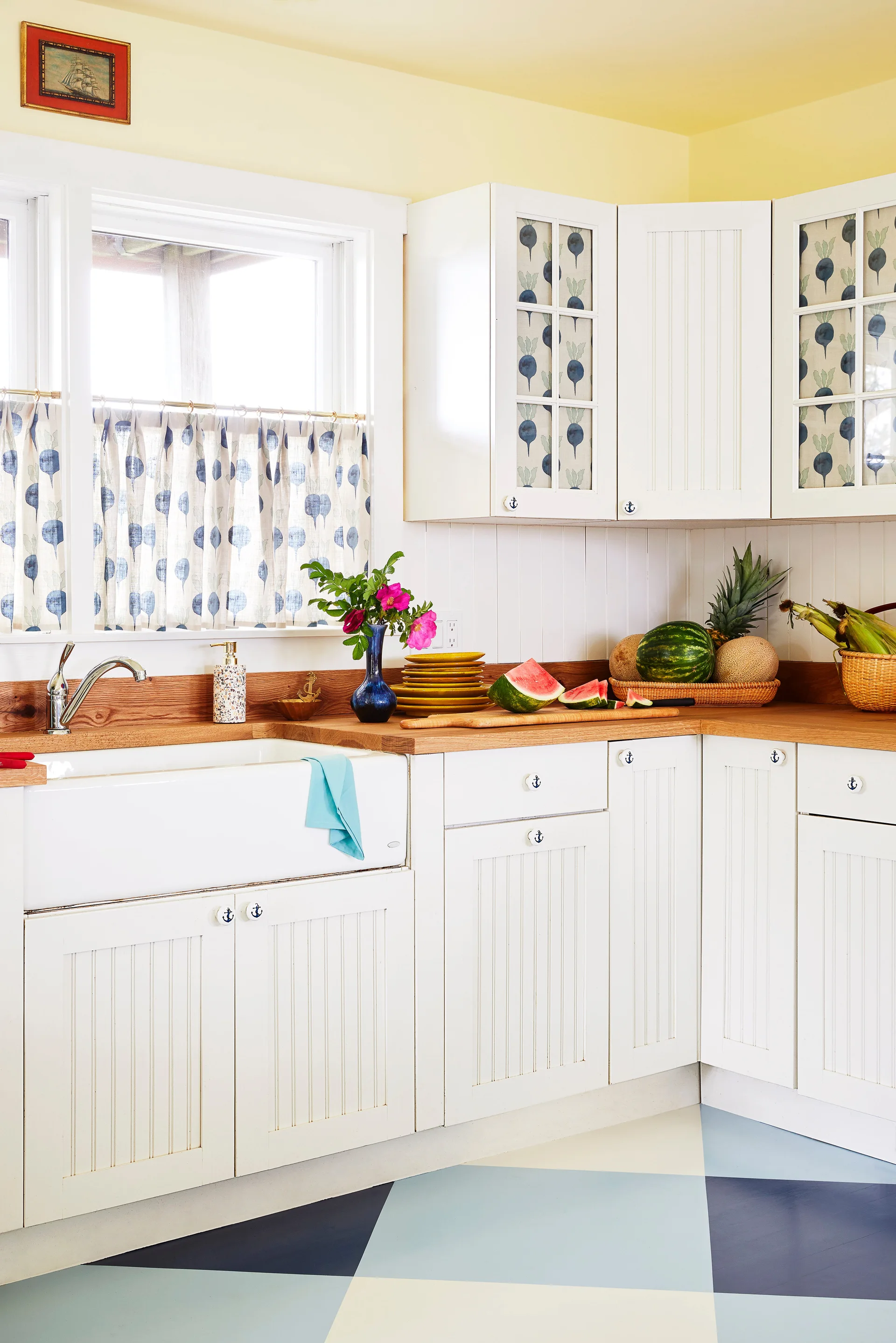 Bright cottage kitchen featuring white beadboard cabinets, wood countertops, an apron sink, and a blue and white geometric painted floor.