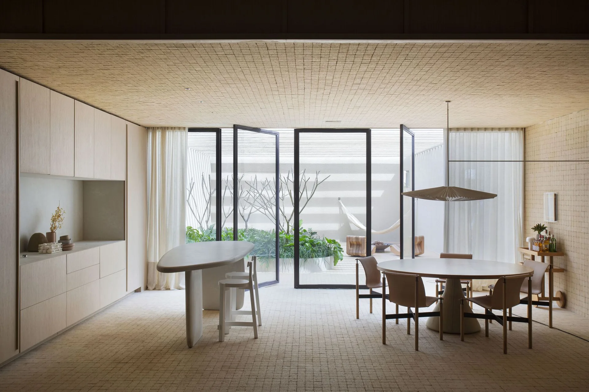 A minimalist dining area with a round wooden table, stone-like island, and continuous beige square tile cladding on the floors, walls, and ceiling.