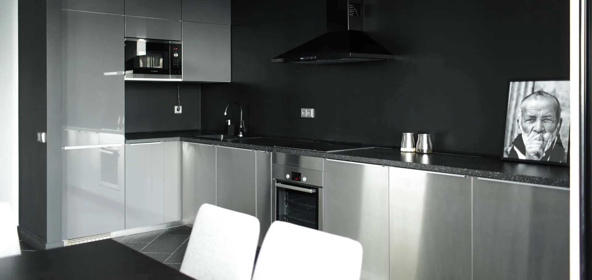 A minimalist kitchen features metallic flat-front cabinetry, a dark speckled countertop, a black range hood, and a matte black wall.