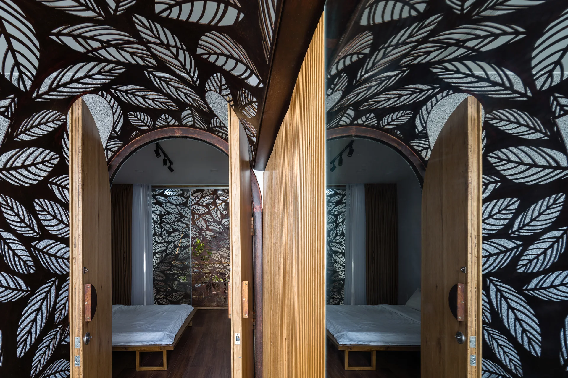 An arched wooden door opens to a bedroom, framed by a dark metal canopy with an intricate laser-cut leaf pattern.