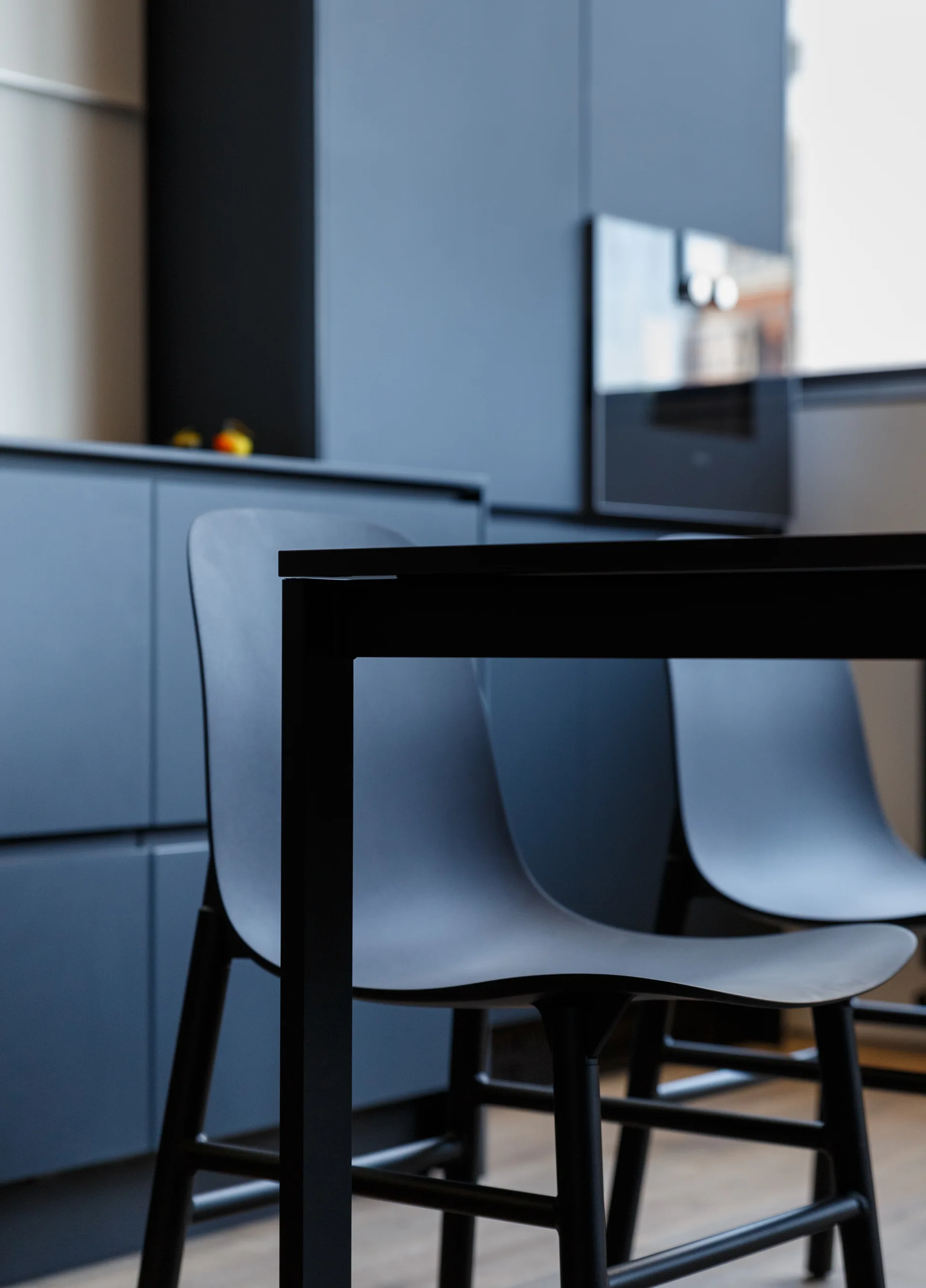 Molded black dining chairs sit at a black table in front of matte dark blue kitchen cabinets.