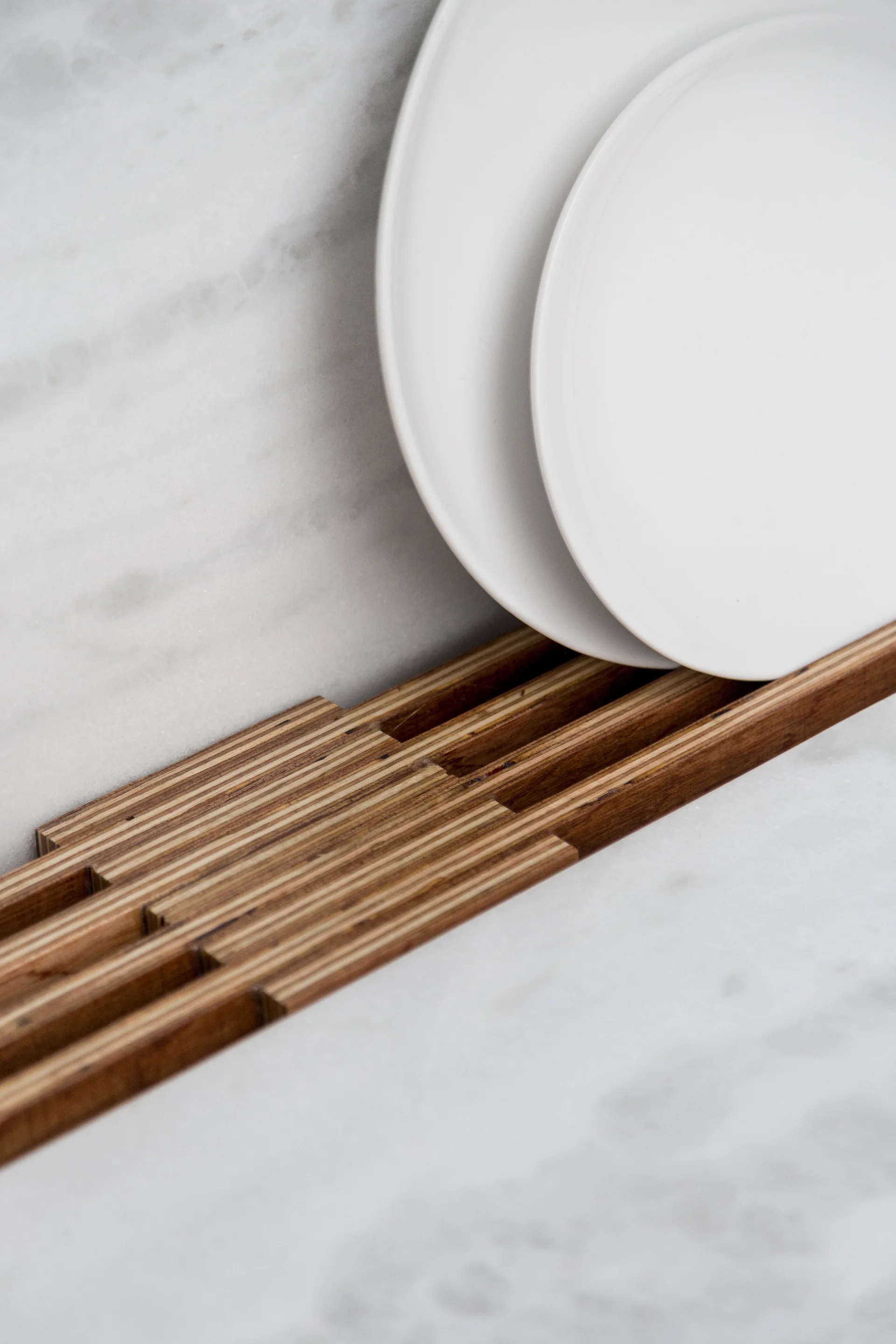 Two matte white plates resting in a slotted plywood plate rack against a veined white marble countertop.