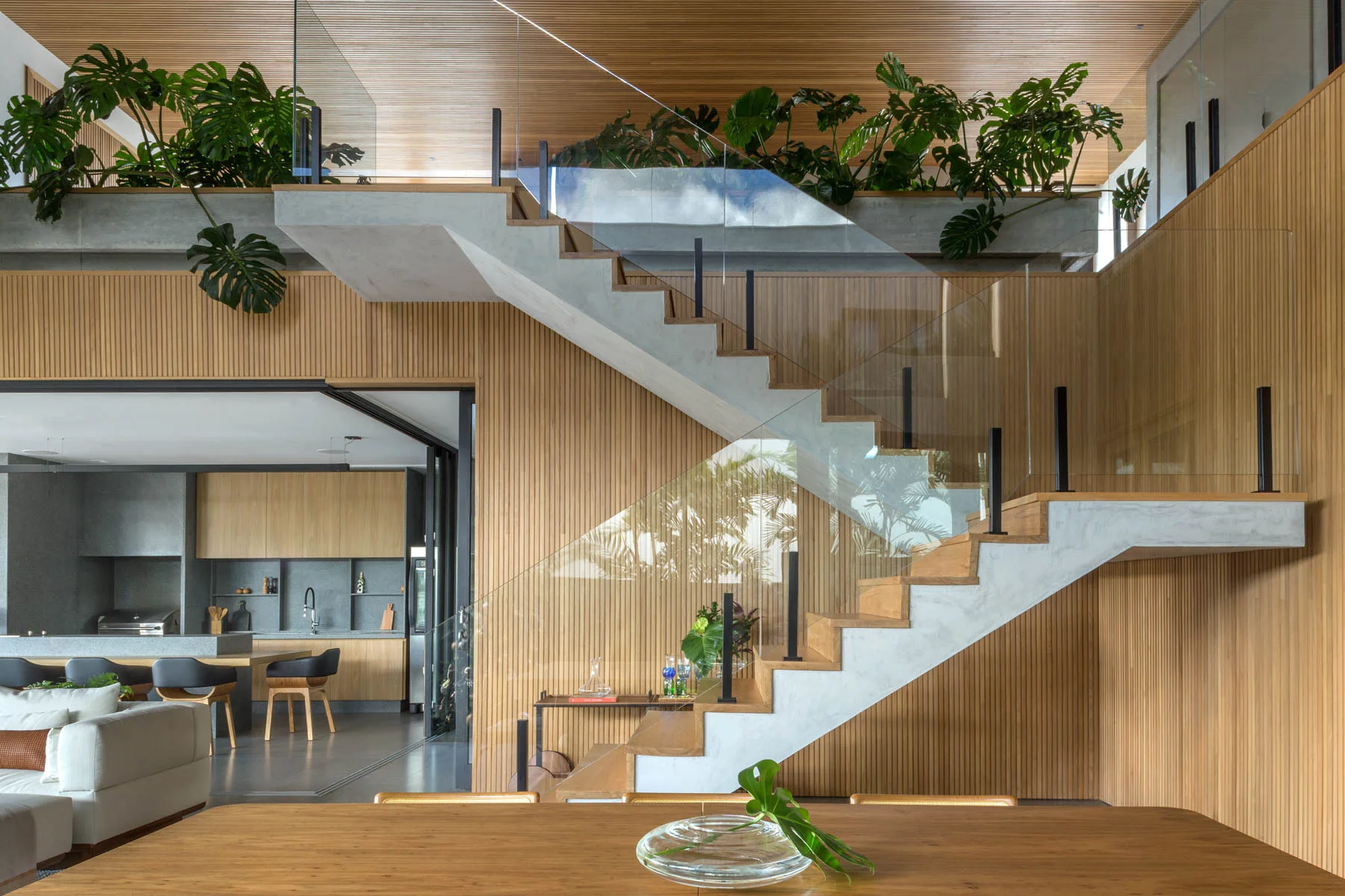 A modern open-concept interior showing a floating concrete and wood staircase with a glass railing against a vertical wood slat wall.