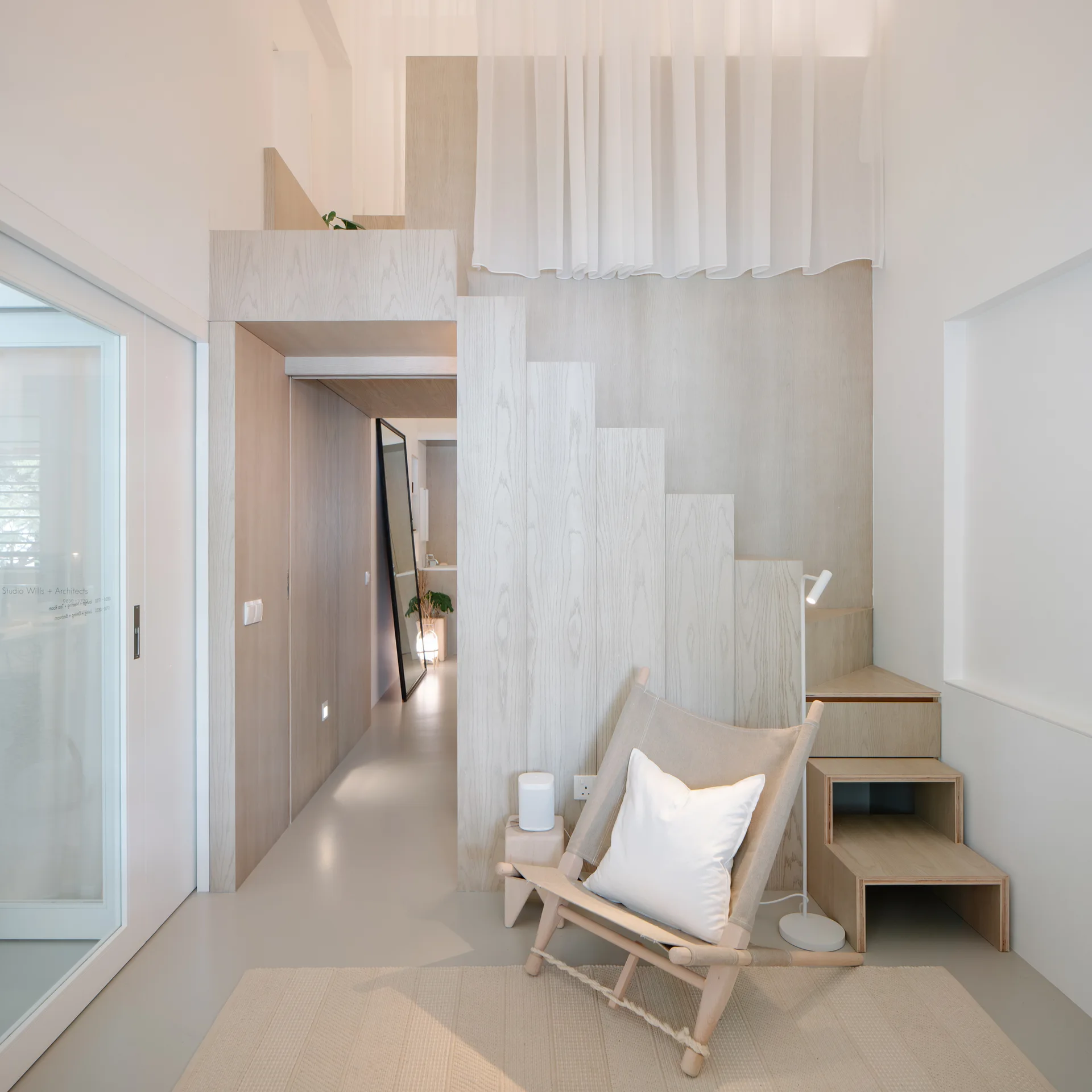 A minimalist living space featuring a light wood staircase integrated into wall paneling beside a canvas lounge chair.