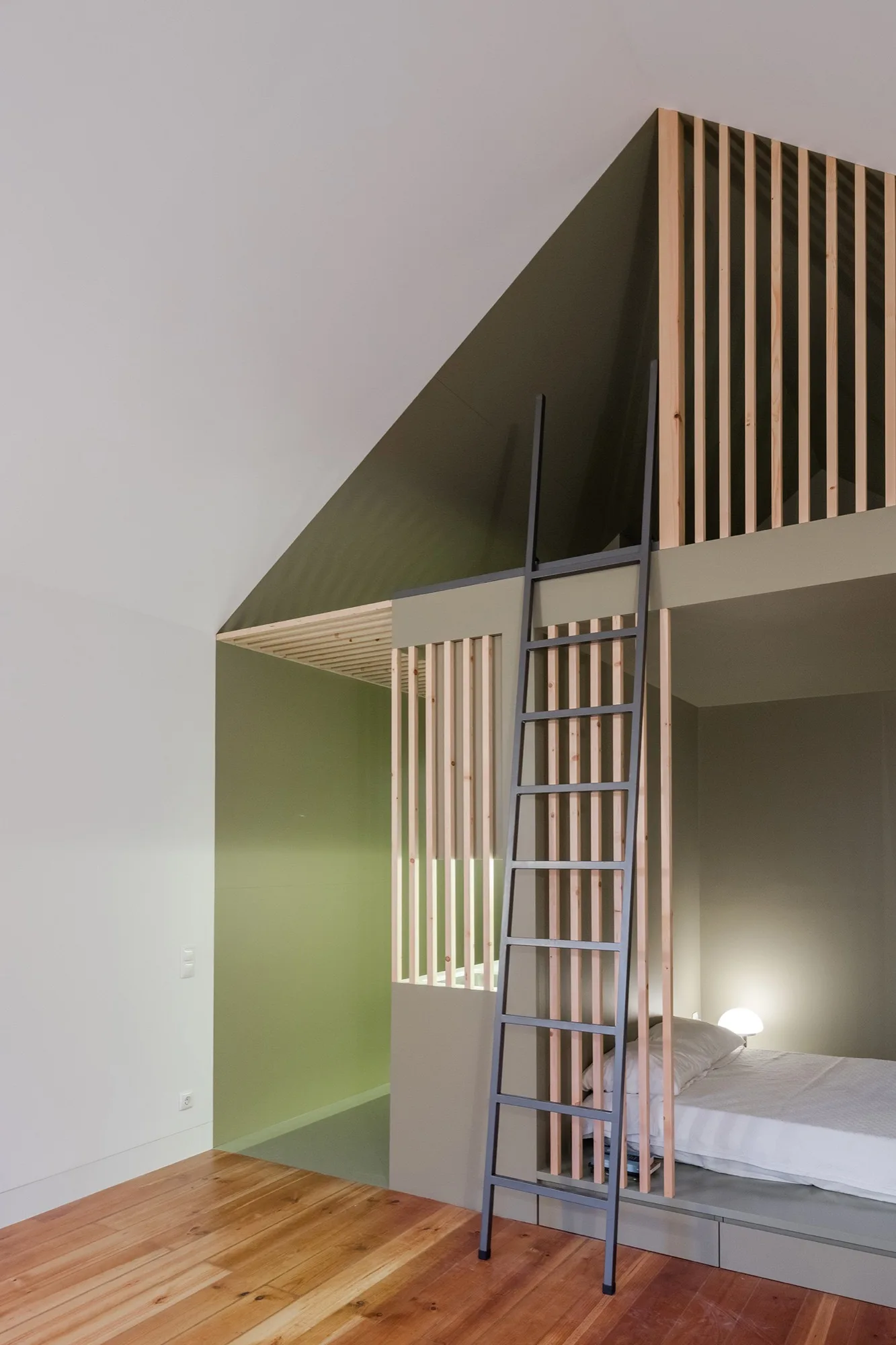 A modern bedroom featuring a custom olive green built-in loft bed with a tall metal ladder, vertical wood slats, and wood plank flooring.