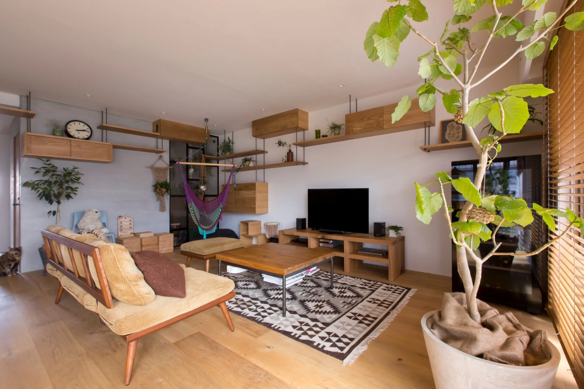 A modern living room features a wooden corduroy sofa, a low wooden coffee table on a patterned rug, and floating wall shelves.