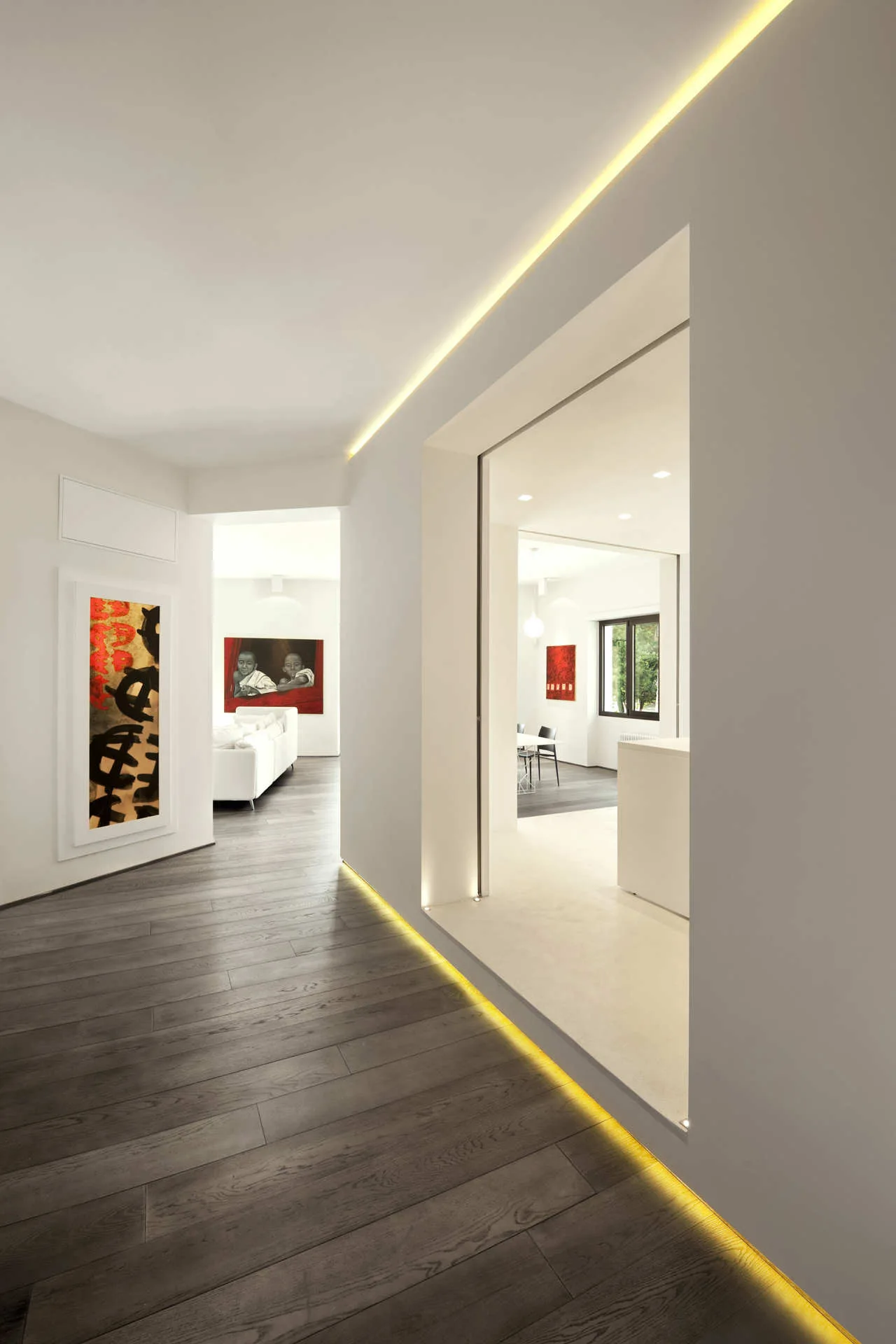 A white minimalist hallway with dark wood floors featuring integrated warm LED strip lighting along the ceiling and floor margins.