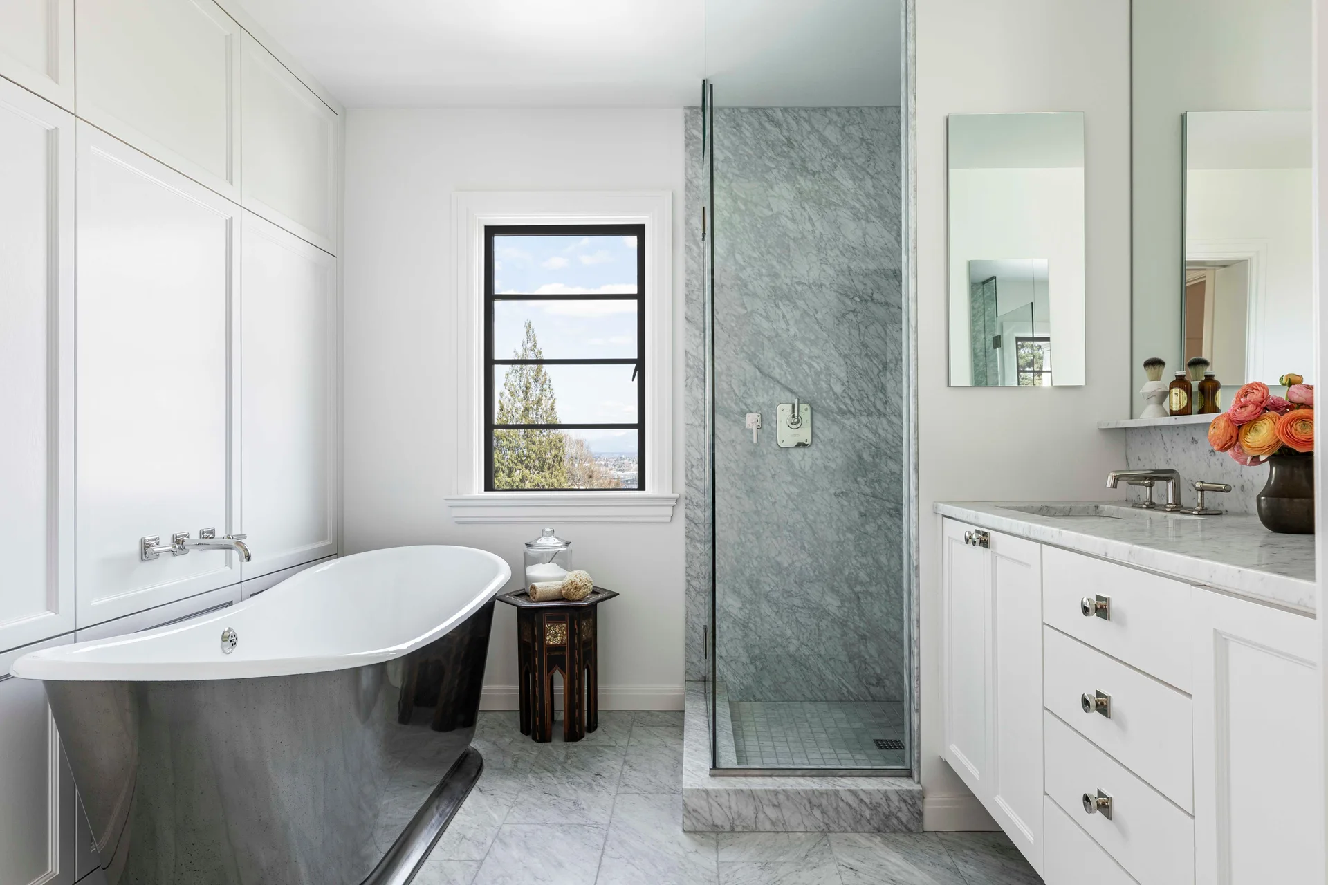 A residential bathroom featuring a metallic freestanding bathtub, white paneled walls, a marble tiled floor, and a glass walk-in shower.