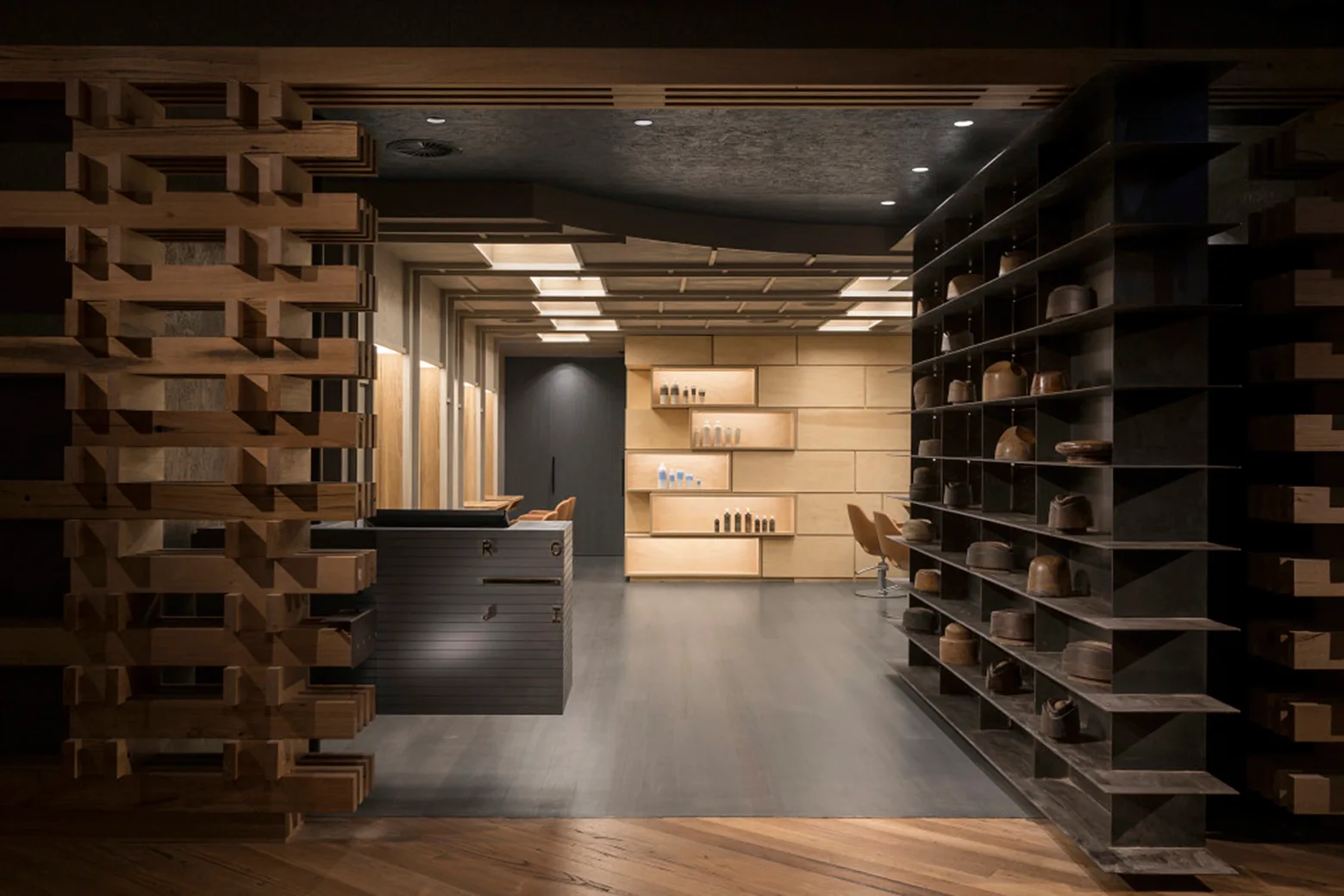 A modern salon reception area featuring a stacked timber partition screen, a dark metal shelving unit, and glowing recessed wall shelves.