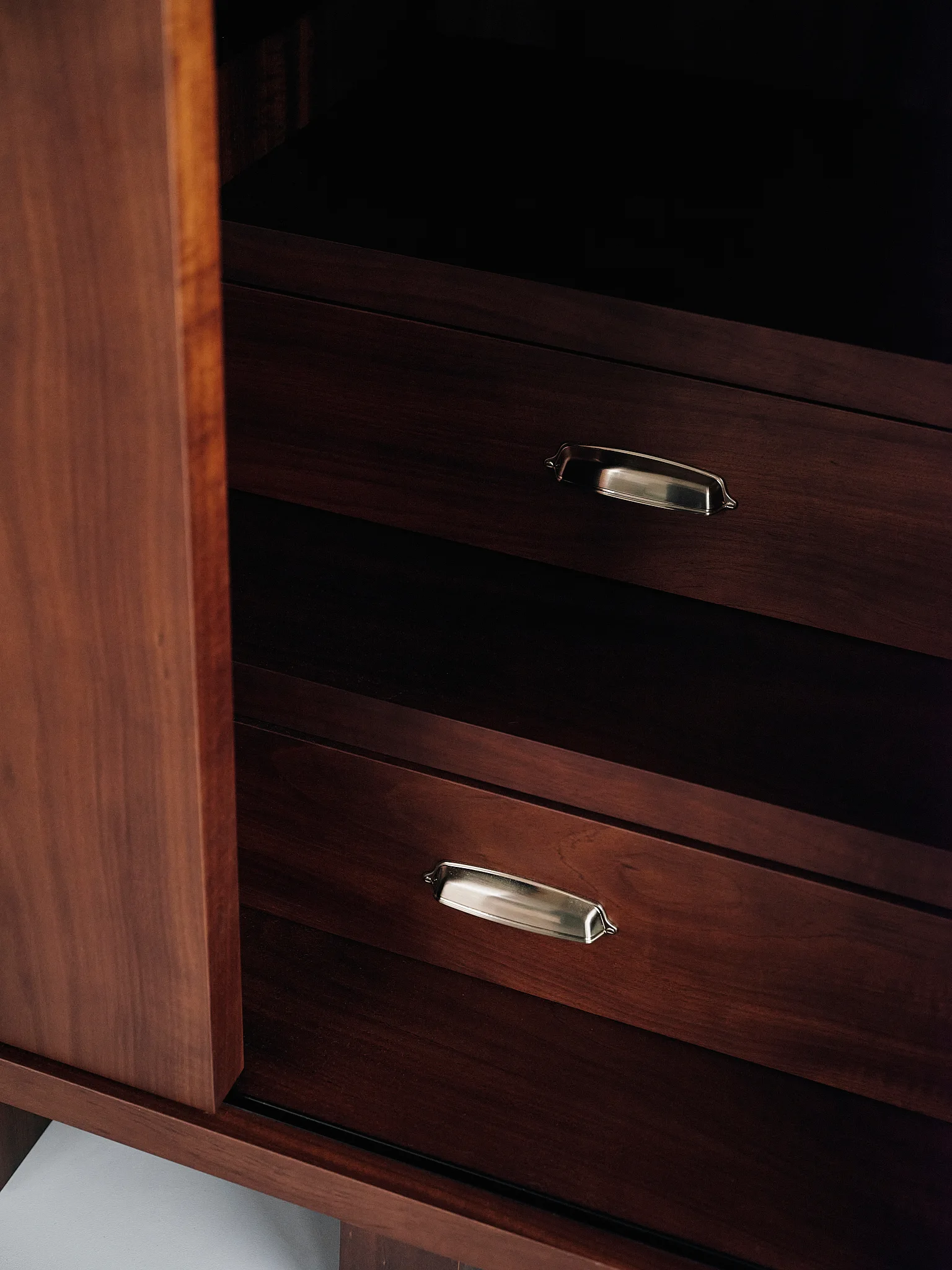 A close-up view of a dark brown wood cabinet interior with two drawers featuring polished silver metal cup pulls.