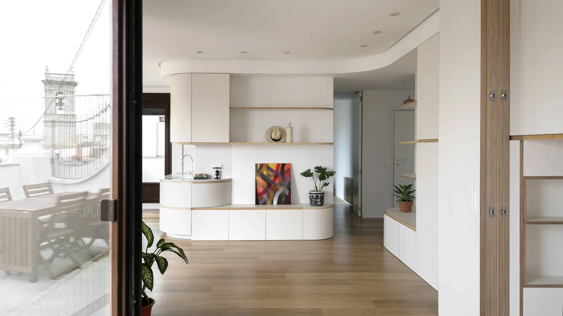 A modern white interior featuring custom cabinetry with light wood accents, hardwood flooring, and a small integrated wet bar.