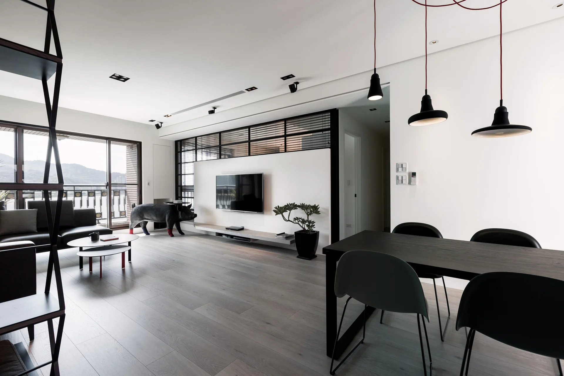 A modern open-concept living and dining area features a wall-mounted TV on a central white partition, a black dining set, and grey wood flooring.