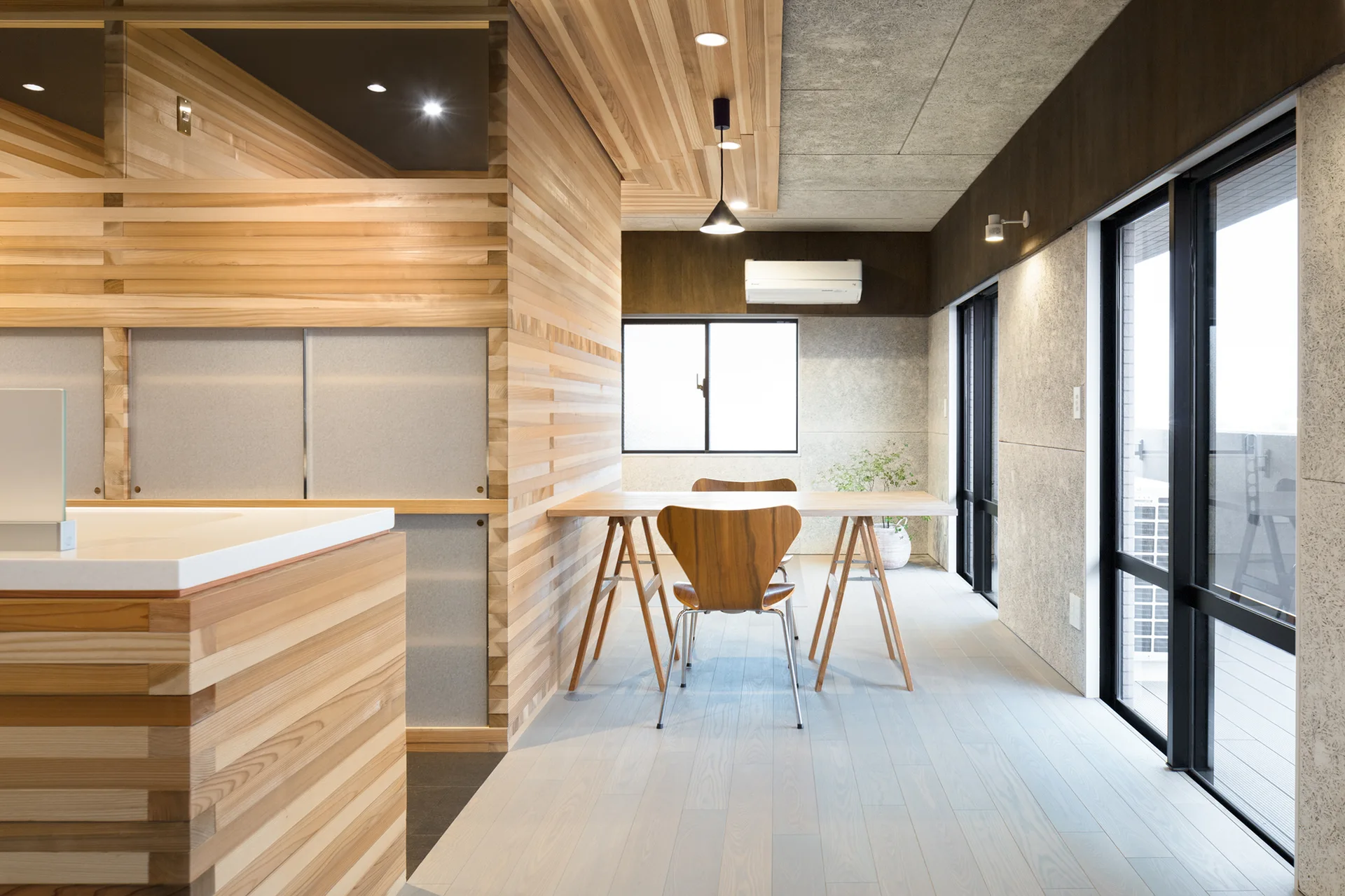 A modern dining space with horizontal wood slat walls, a light wood trestle table, molded plywood chairs, and large glass sliding doors.