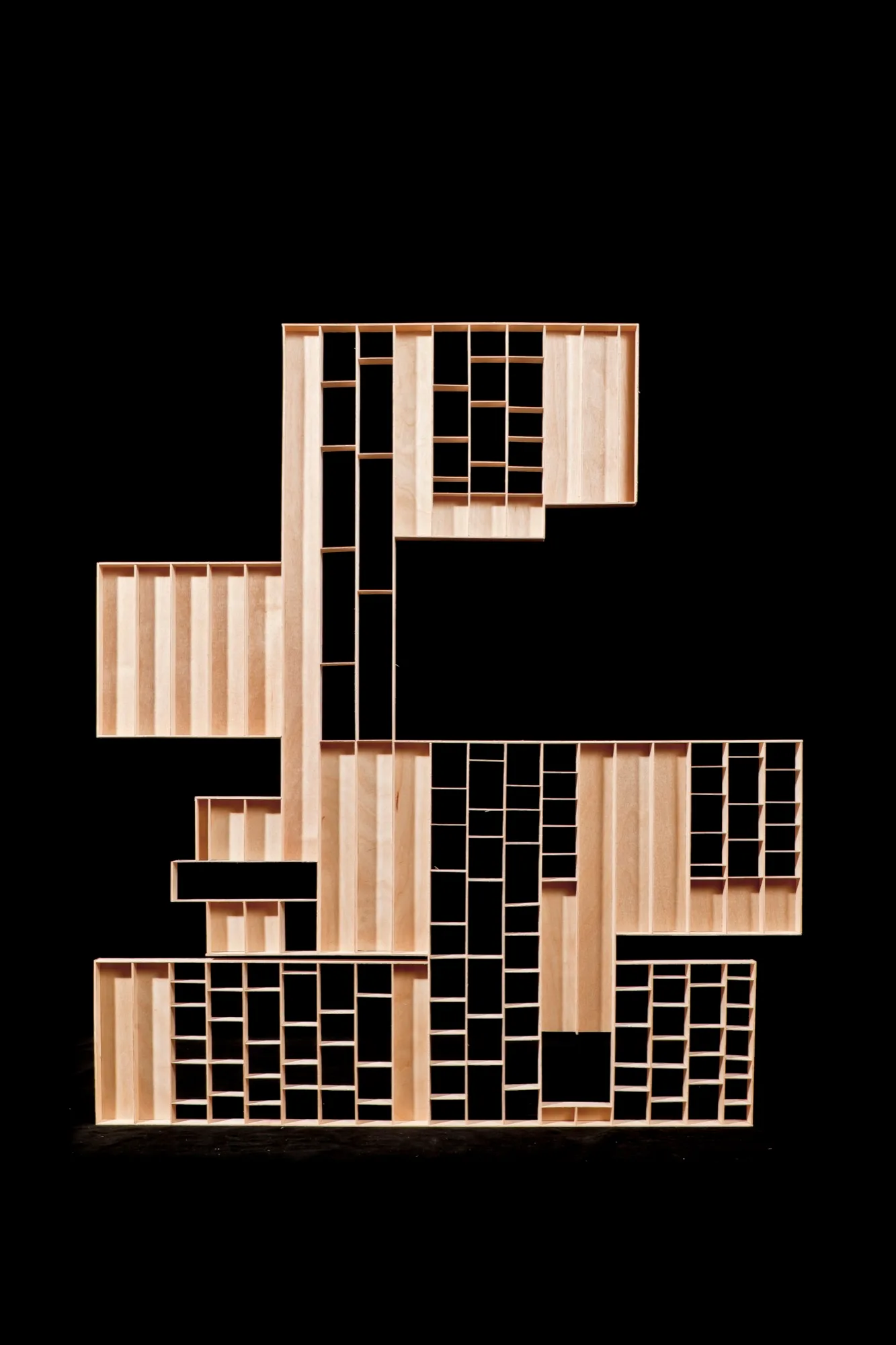 A geometric abstract sculpture made of natural light wood with asymmetrical grids against a solid black background.