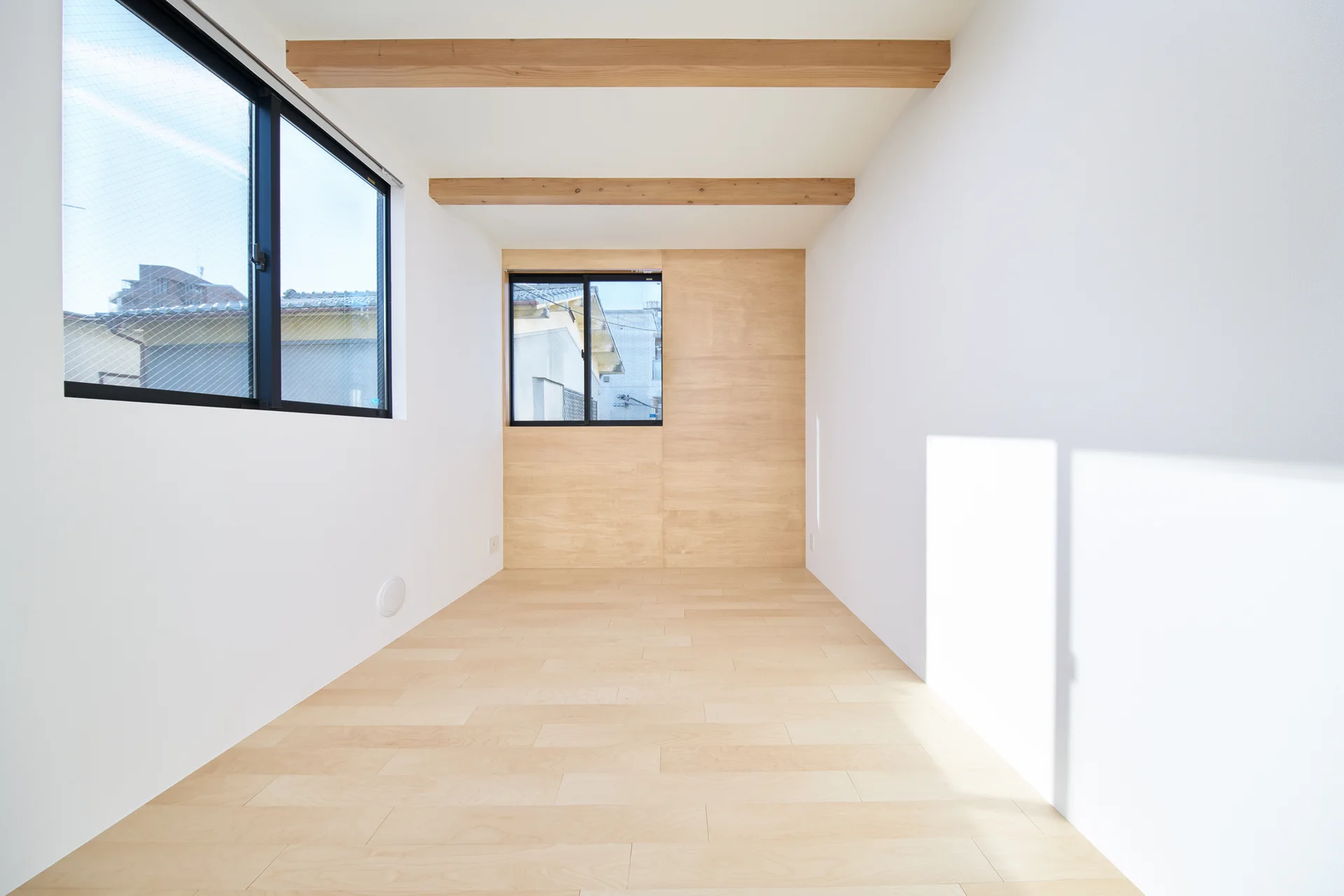An empty minimalist room featuring light wood floors, a matching rear wood panel wall, exposed ceiling beams, and black-framed windows.