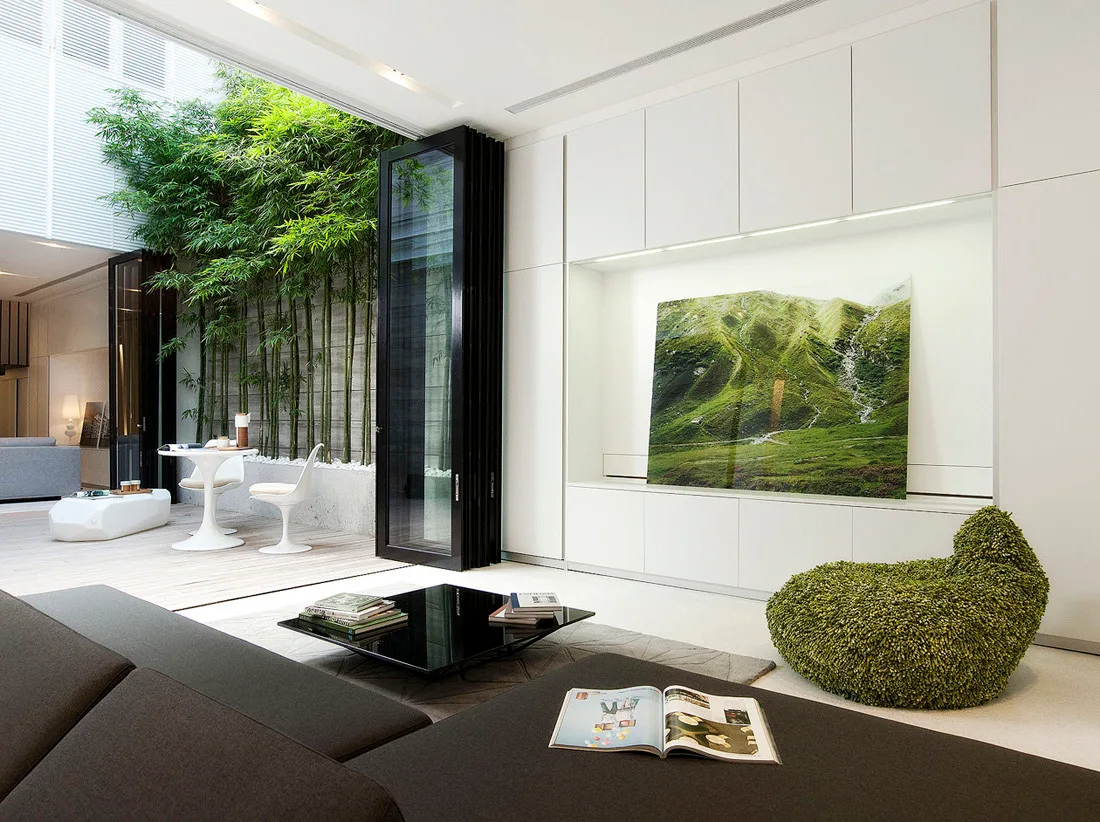 A minimalist white living room features built-in storage and a green textured lounge chair next to glass doors leading to a bamboo courtyard.