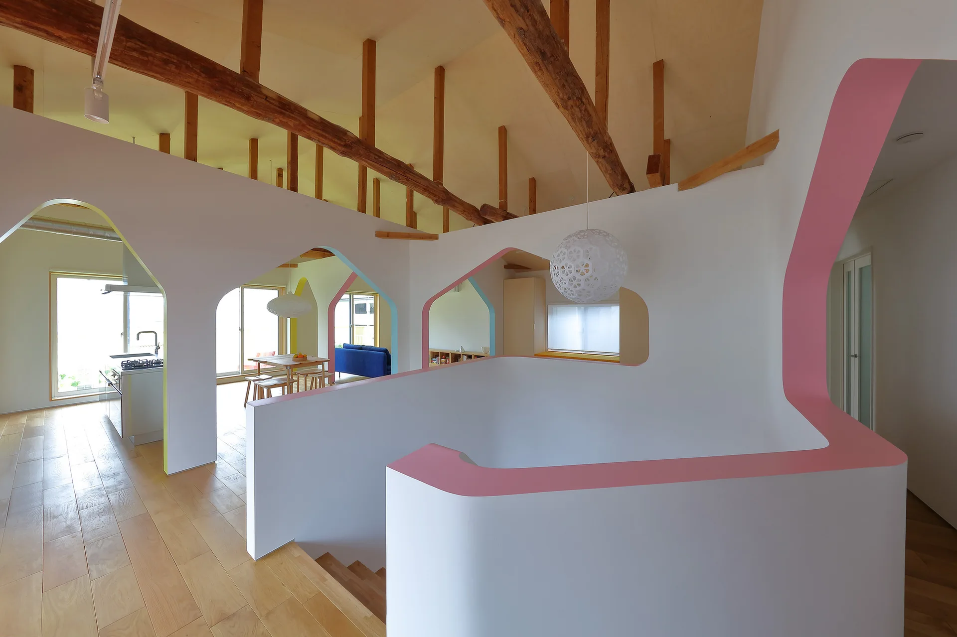 A bright modern interior showing a white staircase with pink trim, architectural archways with colorful borders, and a high ceiling with exposed wood beams.