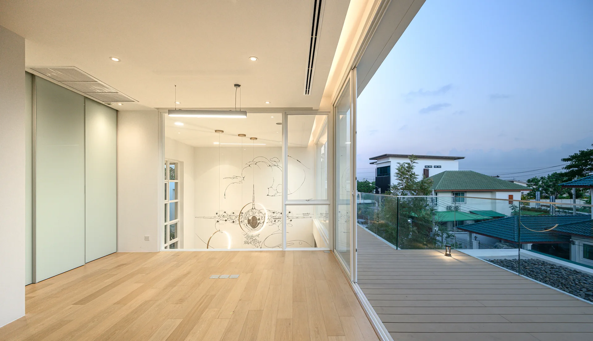 An empty minimalist interior with light wood flooring, a pale green sliding wardrobe, and large glass doors leading to a wooden deck balcony.