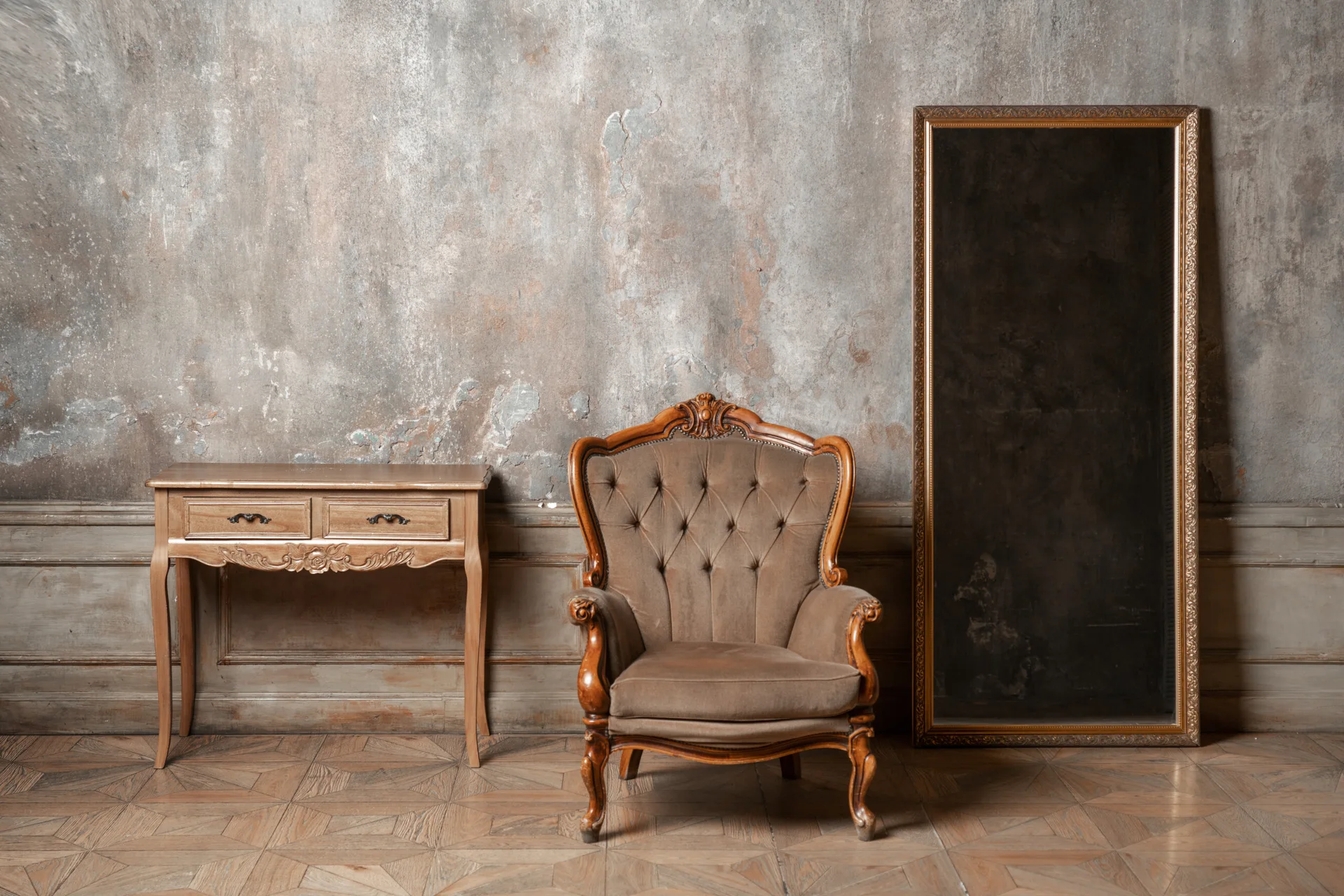 A tufted brown armchair sits between a wooden console table and a large floor mirror against a weathered plaster wall over wood wainscoting.