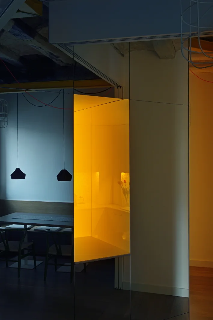 A modern dining room features a table with chairs, black pendant lights, and a large mirrored partition reflecting a bright yellow room.