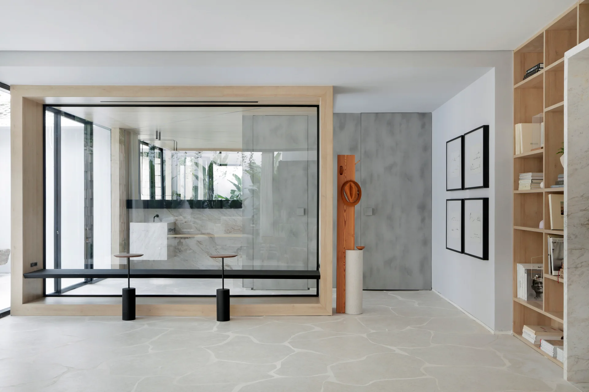 A minimalist hallway featuring an irregular stone floor, a large wood-framed glass partition, a built-in bookshelf, and framed artwork on the wall.