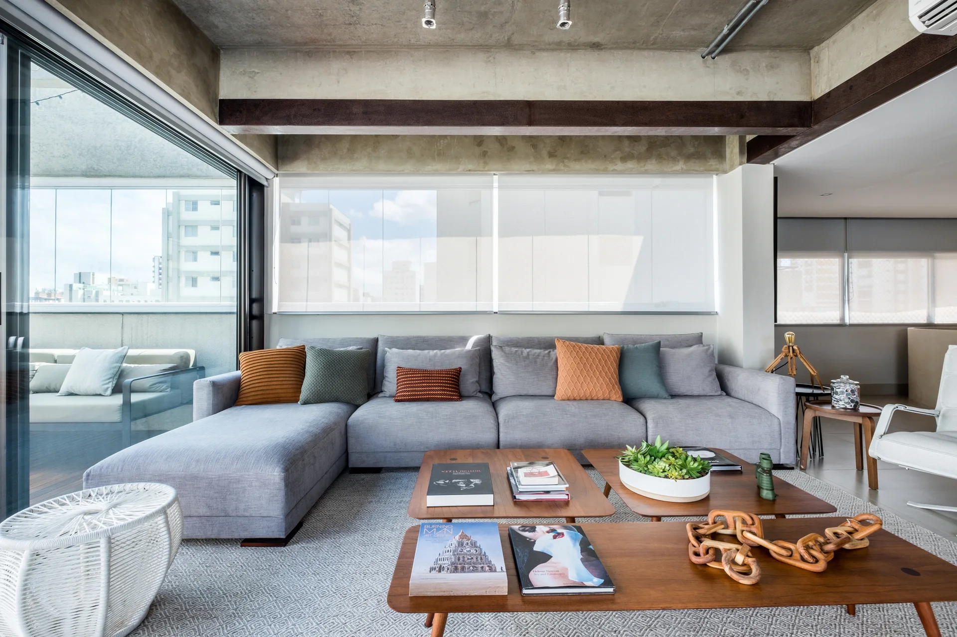 A grey sectional sofa sits on a geometric rug beneath an exposed concrete ceiling in an industrial-style living room with wooden coffee tables.