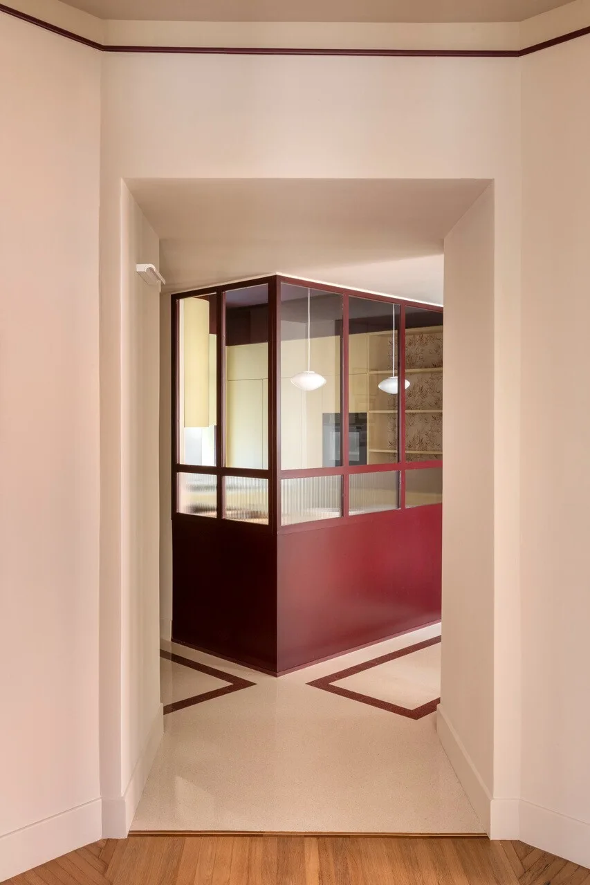 A framed view from a hallway looking towards a cream room featuring a geometric floor design and a burgundy glass partition.