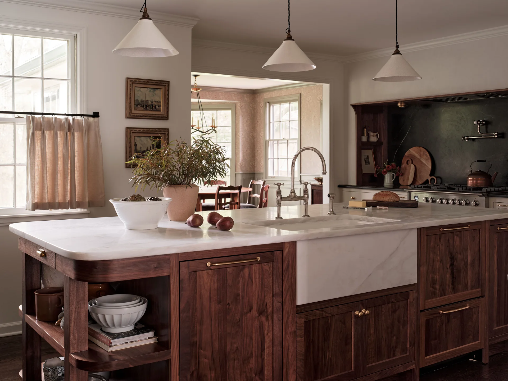 A walnut kitchen island features a white marble countertop with an integrated farmhouse sink, illuminated by three white pendant lights.