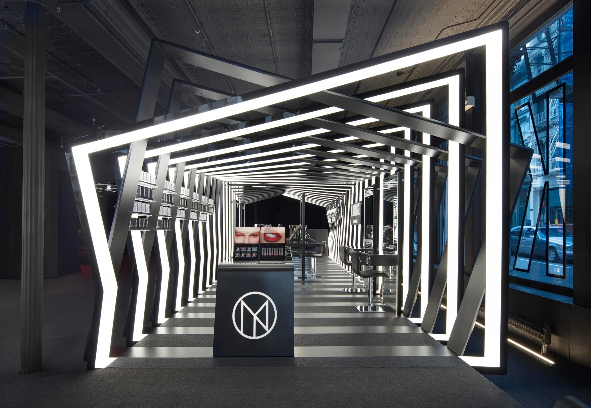 A modern commercial retail space featuring a geometric light tunnel of glowing white LED frames over a bold black and white striped floor.