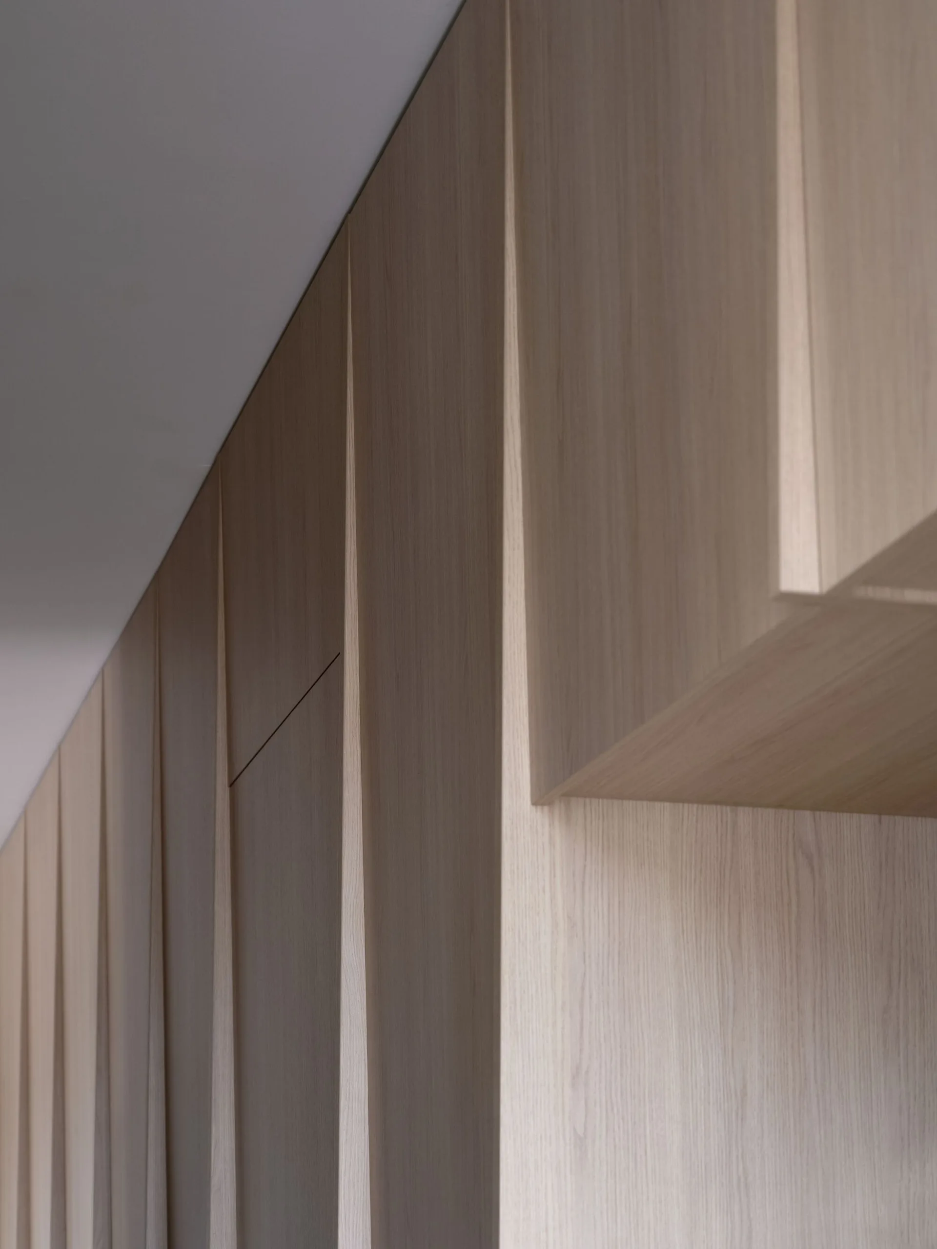 A close-up view of custom built-in wood cabinetry featuring light beige vertical panels and seamless flush joints.