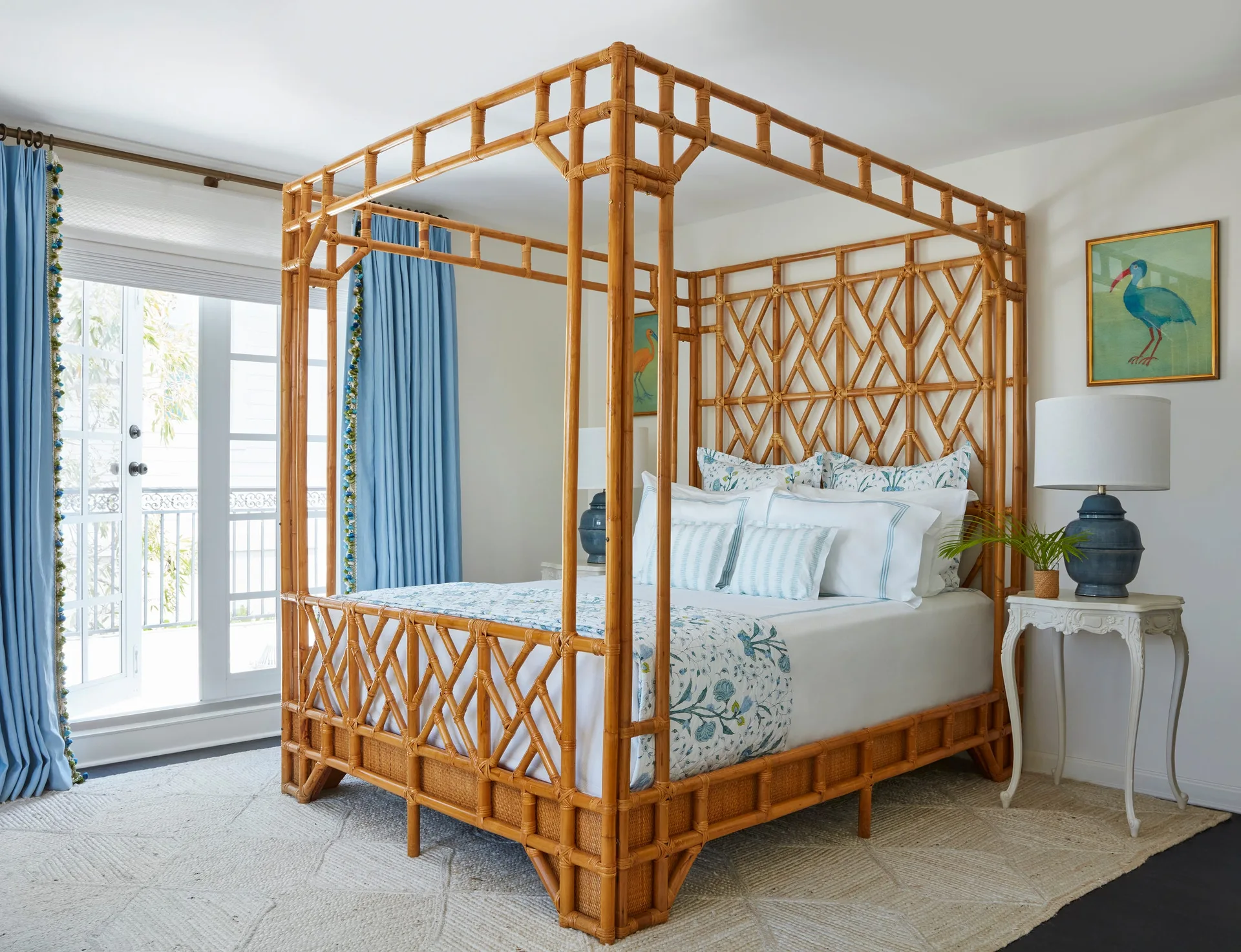 A bedroom features a prominent bamboo canopy bed styled with blue patterned bedding, flanked by white side tables with blue ceramic lamps.