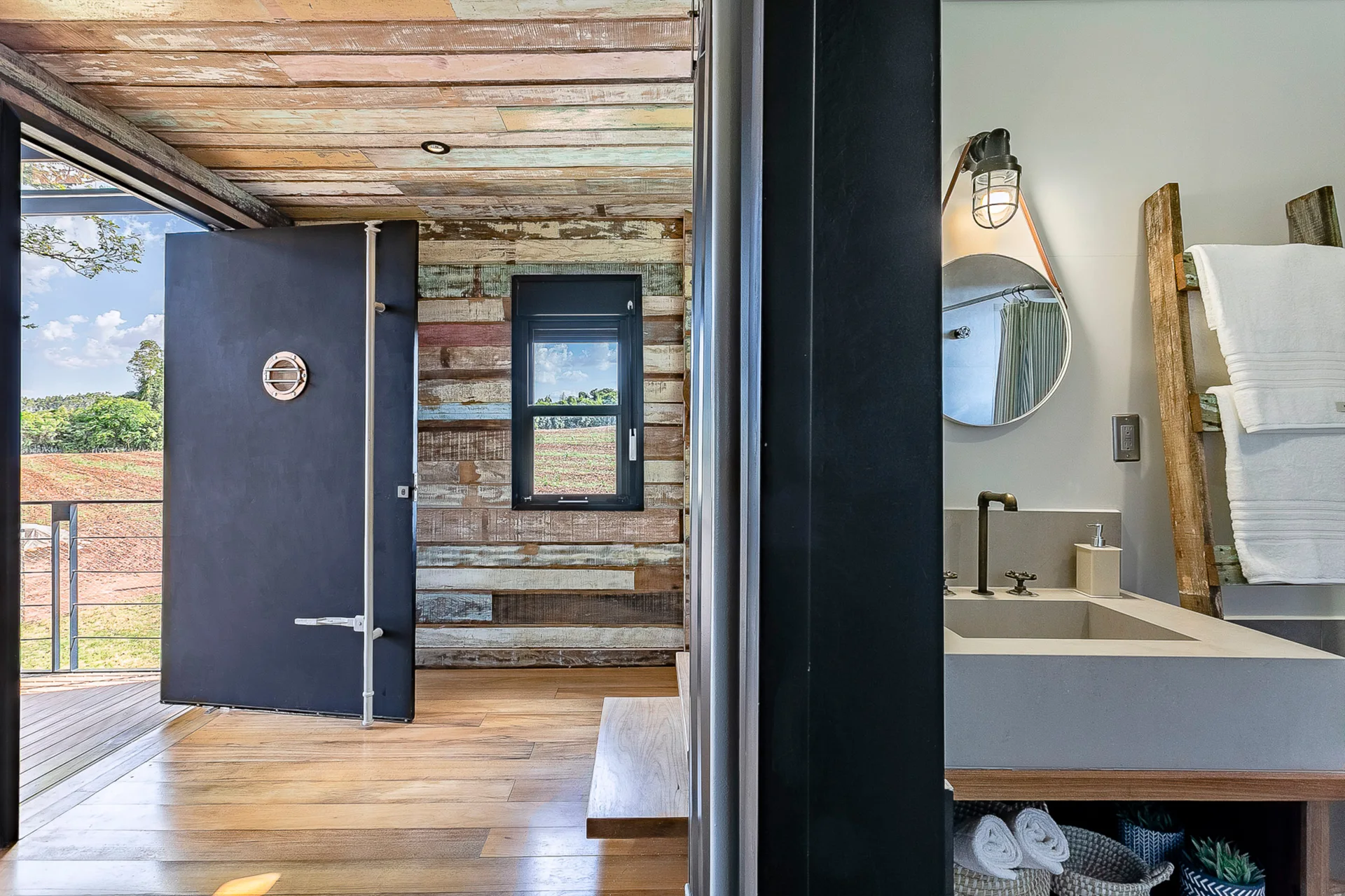 A modern bathroom with a grey concrete vanity next to an entryway featuring multicolored reclaimed wood walls and a large black pivot door.
