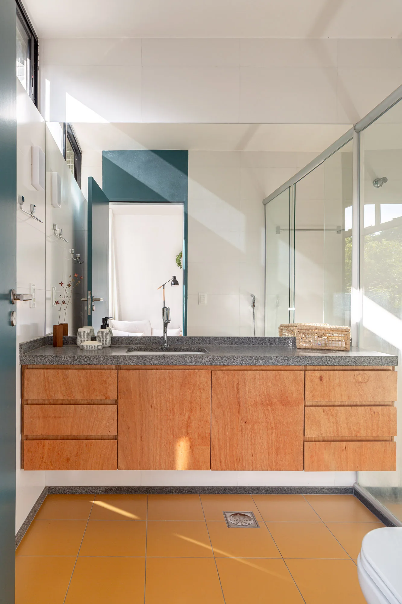 A modern bathroom featuring a floating wood vanity with a grey stone countertop, large wall mirror, and mustard yellow floor tiles.