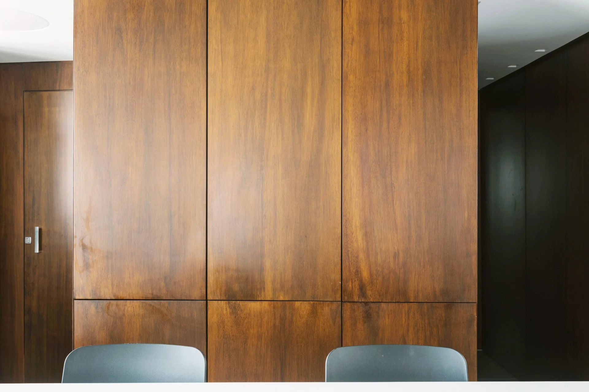 Floor-to-ceiling vertical wood panels in a warm brown stain line a wall, featuring a matching integrated flush door with a slim metal handle.