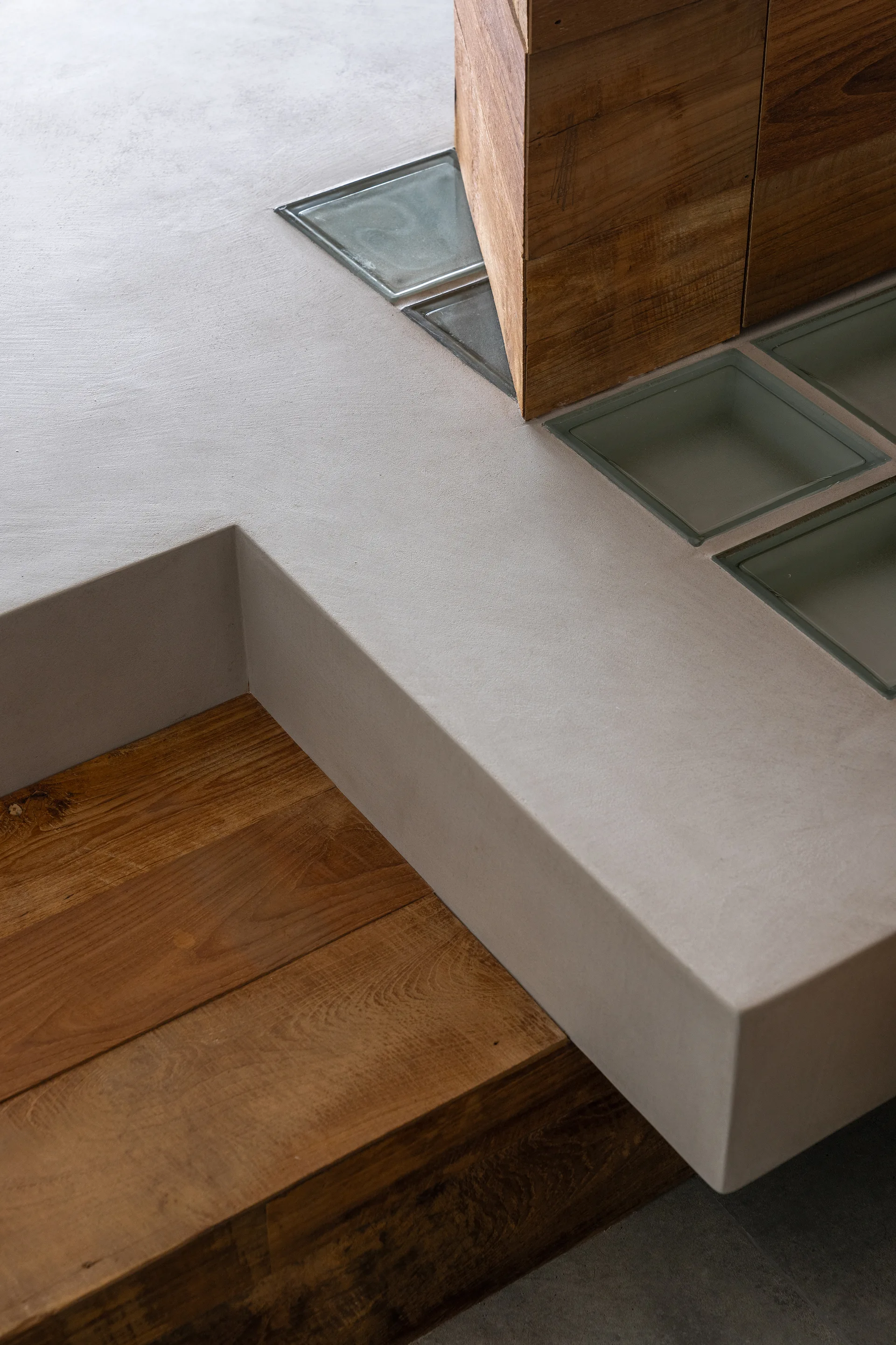 A close-up of a smooth grey concrete platform step meeting warm wooden planks with a row of inset glass blocks.
