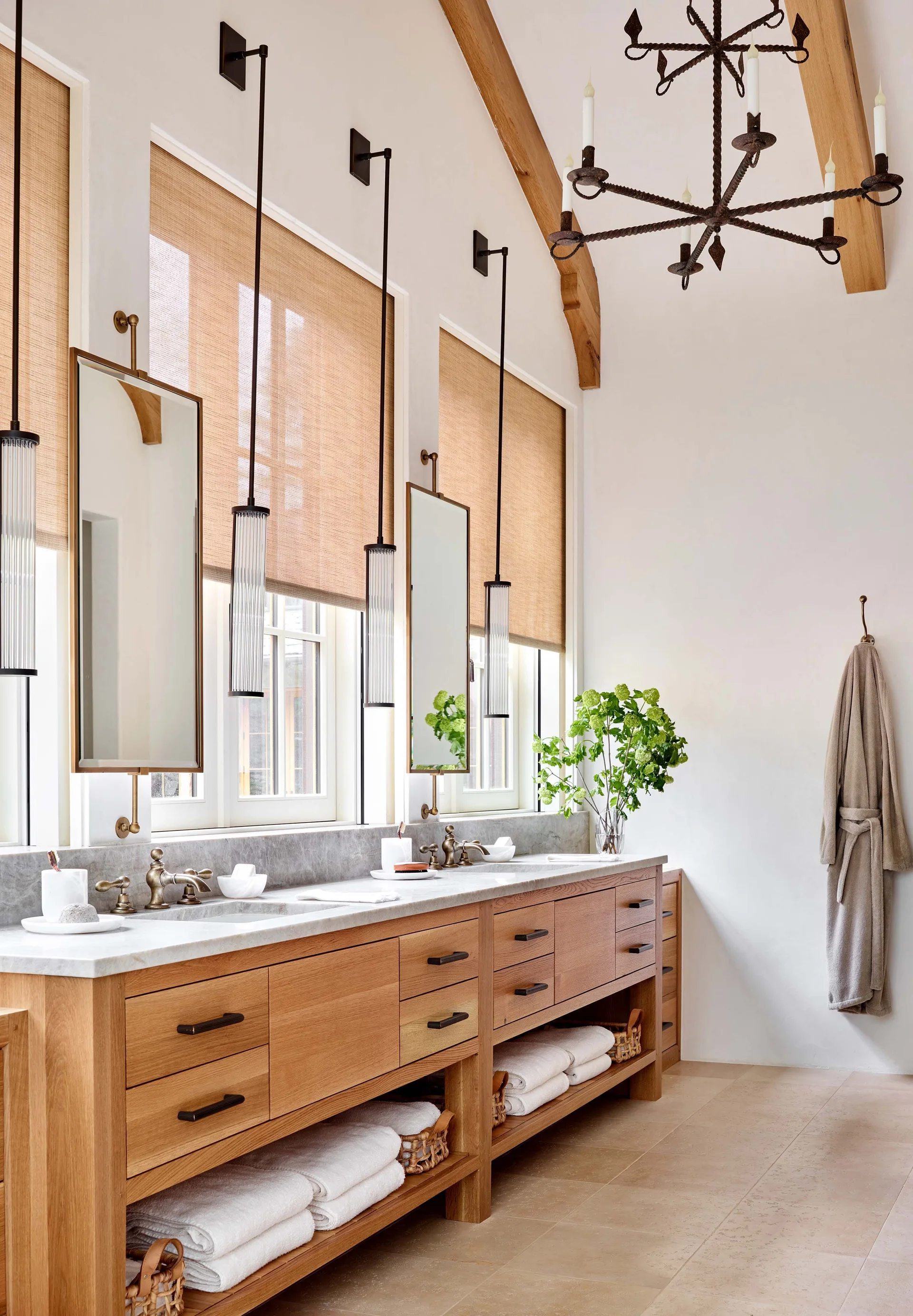 A rustic-modern bathroom features a long light oak double vanity with a stone countertop, rectangular hanging mirrors, and woven window shades.
