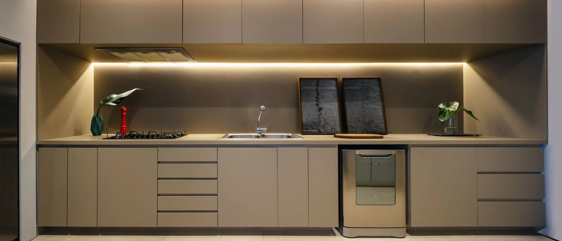 A minimalist kitchen workspace featuring matte taupe slab cabinets, under-counter integrated lighting, and a stainless steel sink.