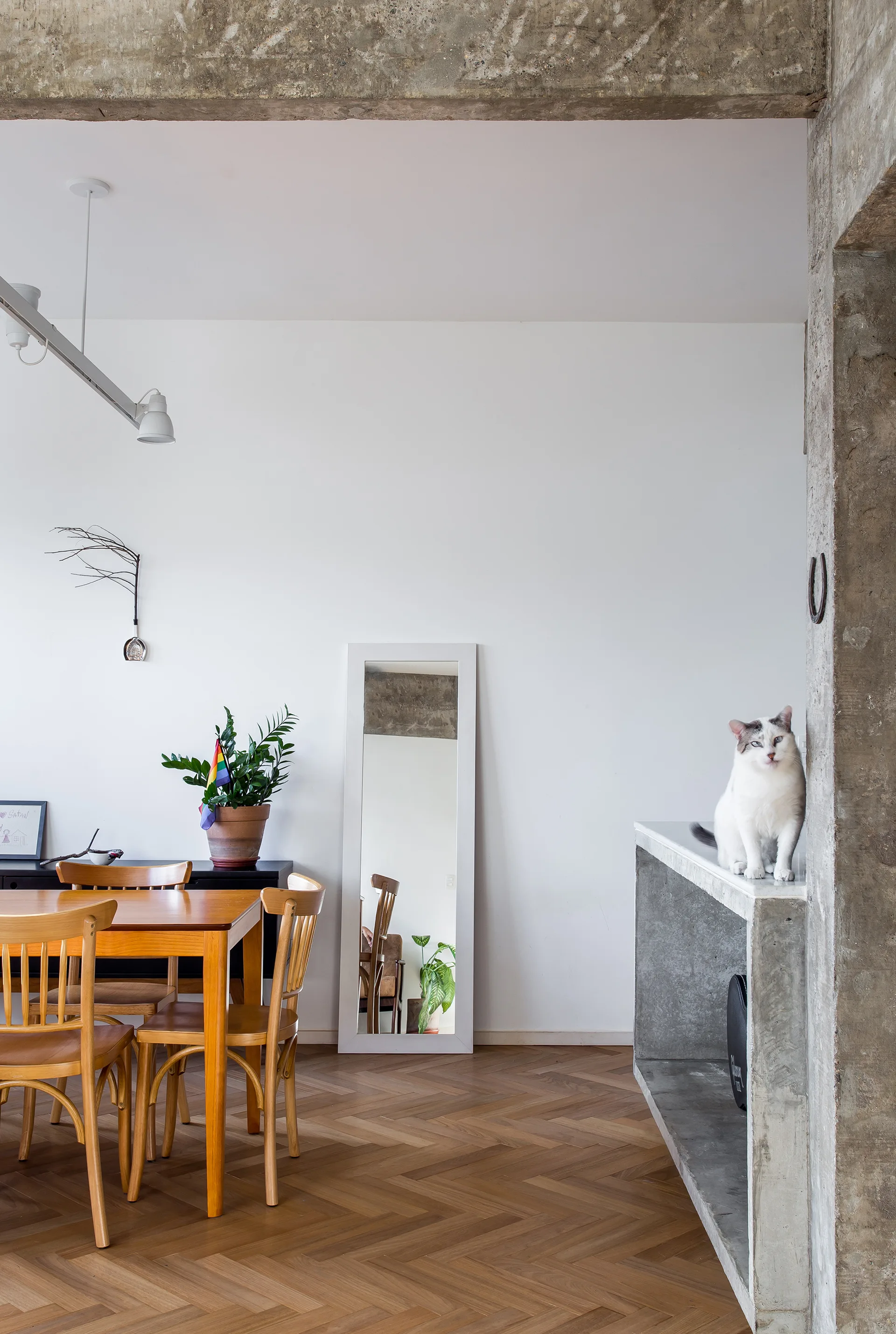 A dining room features a wooden table and chairs on herringbone flooring beneath an exposed concrete beam.