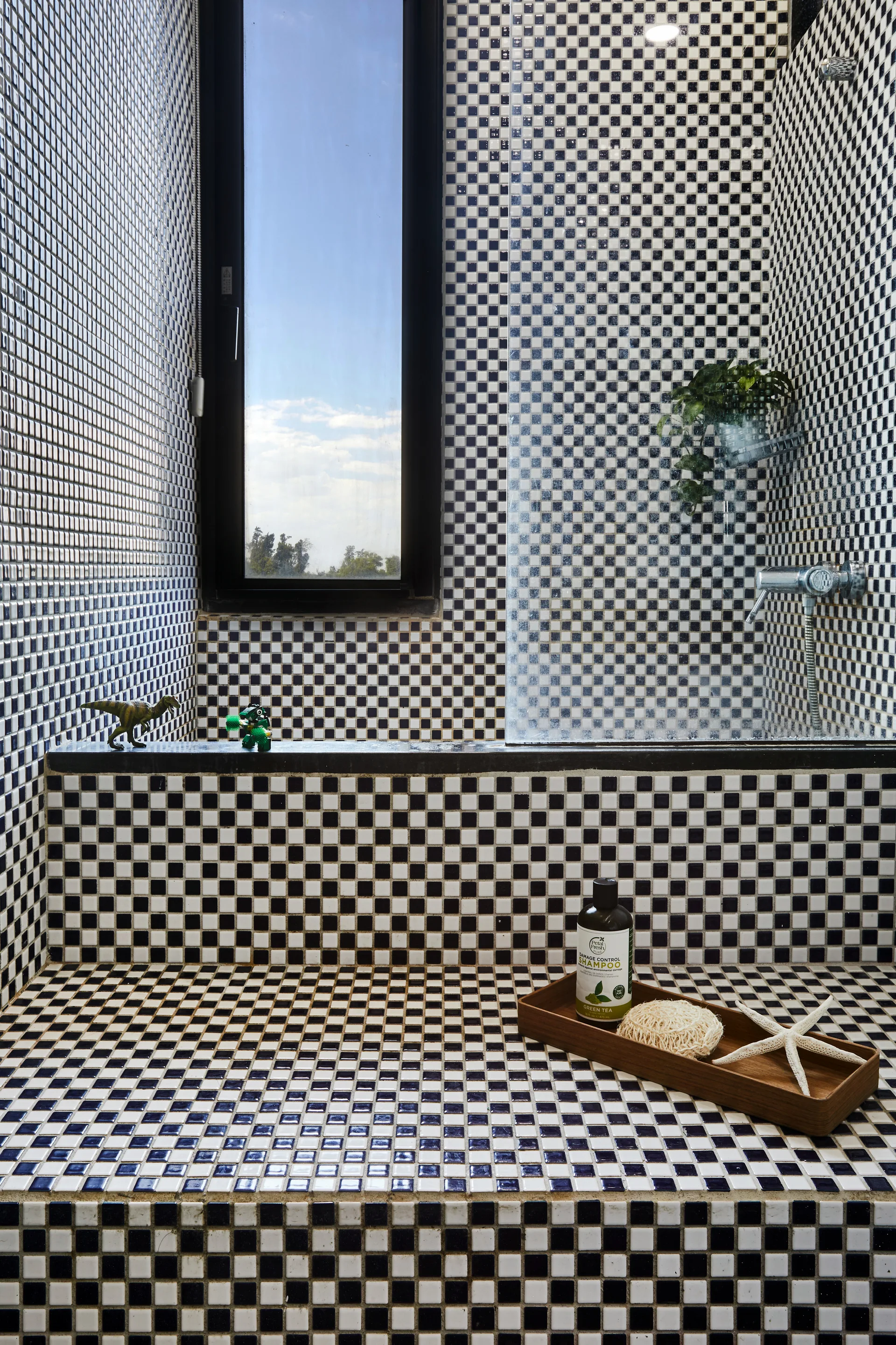 A modern shower featuring black and white checkerboard mosaic tiles on the walls and bench with a tall vertical window.