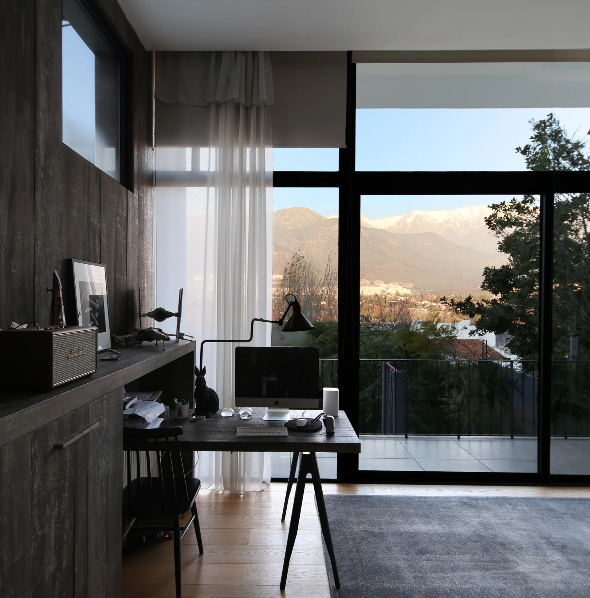 A sleek workspace featuring a dark wooden desk and built-in cabinetry beside a large window overlooking a snow-capped mountain range.