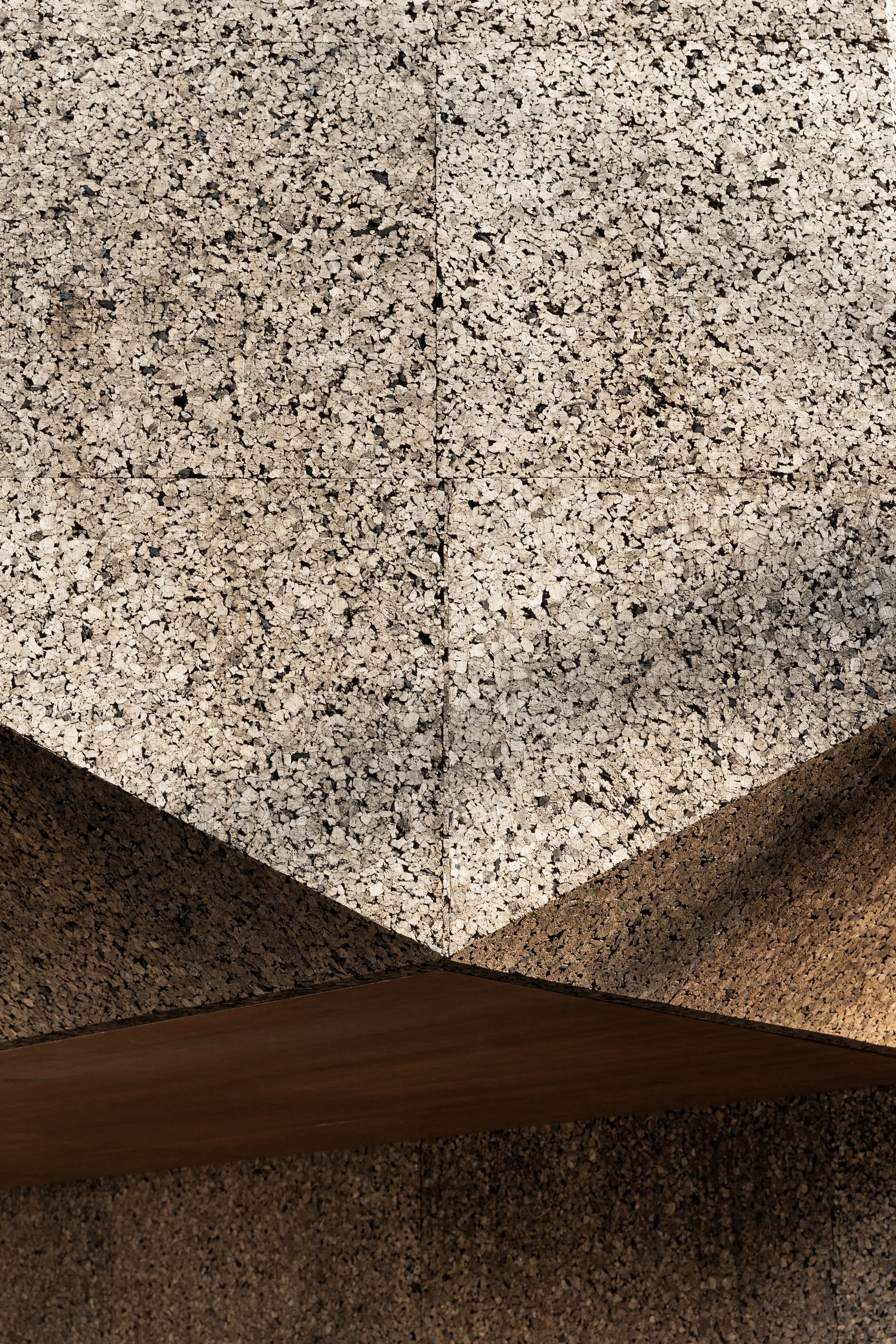 An extreme close-up of granular tan cork panels arranged in a sharp geometric pattern with shadow casting over the angled surfaces.