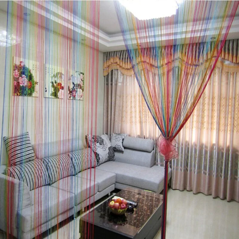 A grey sectional sofa and dark coffee table sit behind a vibrant rainbow-colored string curtain partition in a neutral living room.