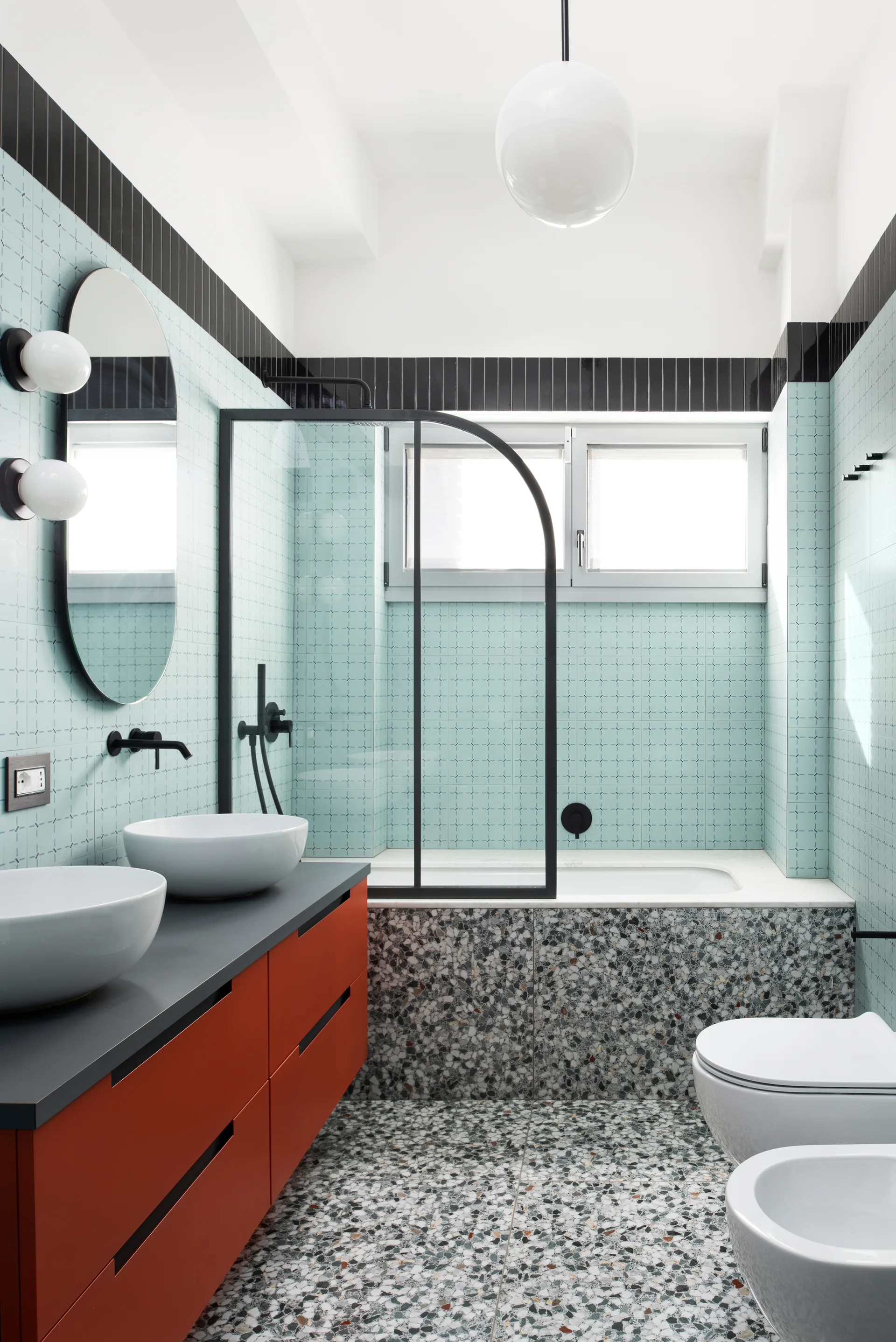 A contemporary bathroom features a matte orange double vanity, light blue patterned wall tiles, and a terrazzo floor and bathtub surround.
