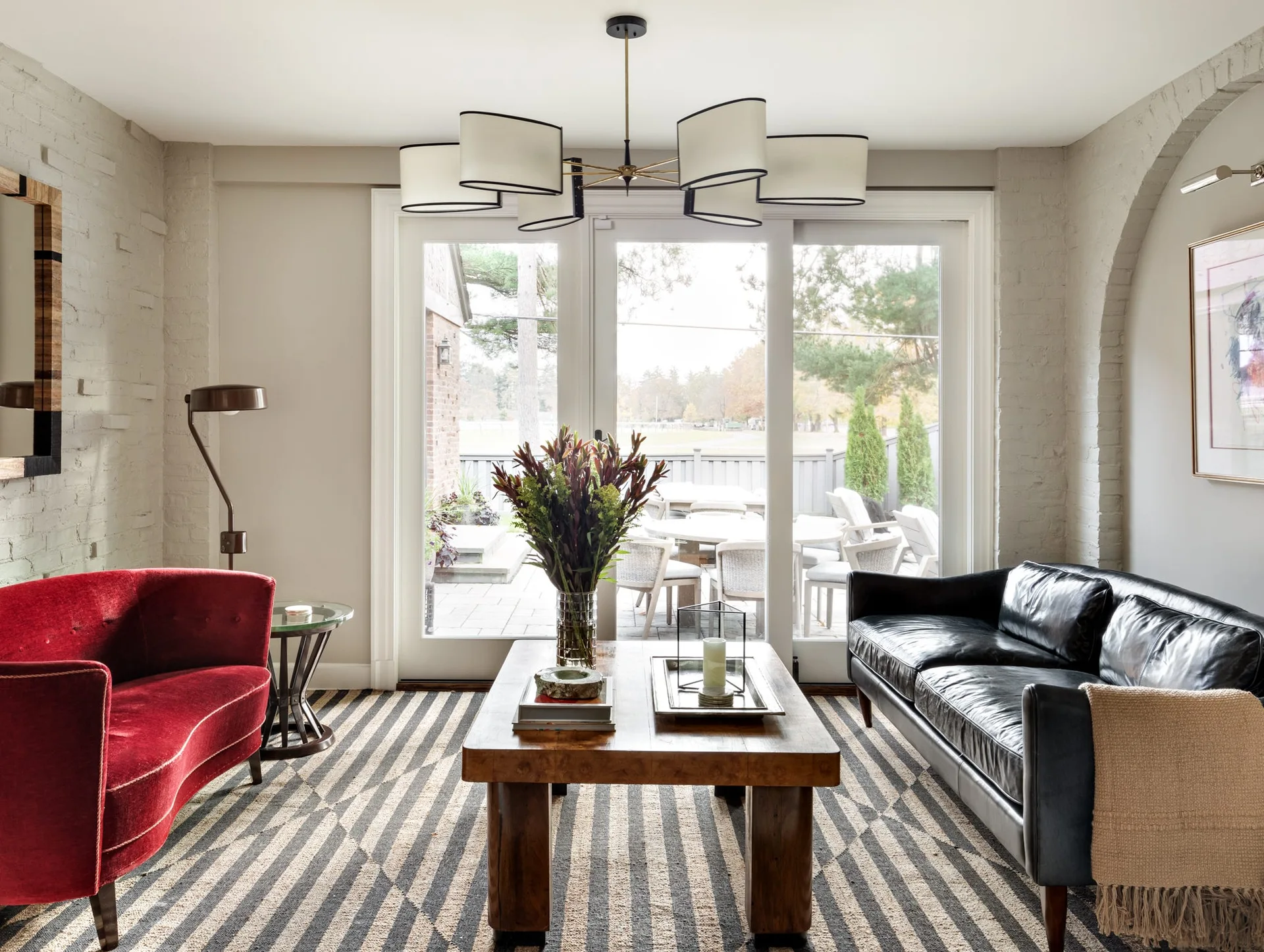 A transitional living room features a red velvet sofa and a black leather sofa facing a wood coffee table on a bold black and white striped area rug.
