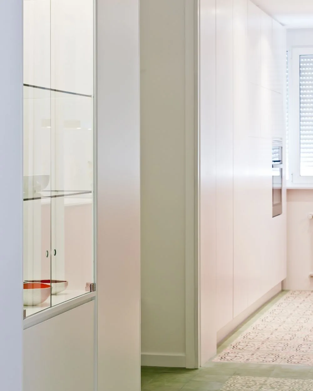 A modern kitchen featuring floor-to-ceiling white cabinetry, an integrated oven, a glass display case, and patterned tile flooring.