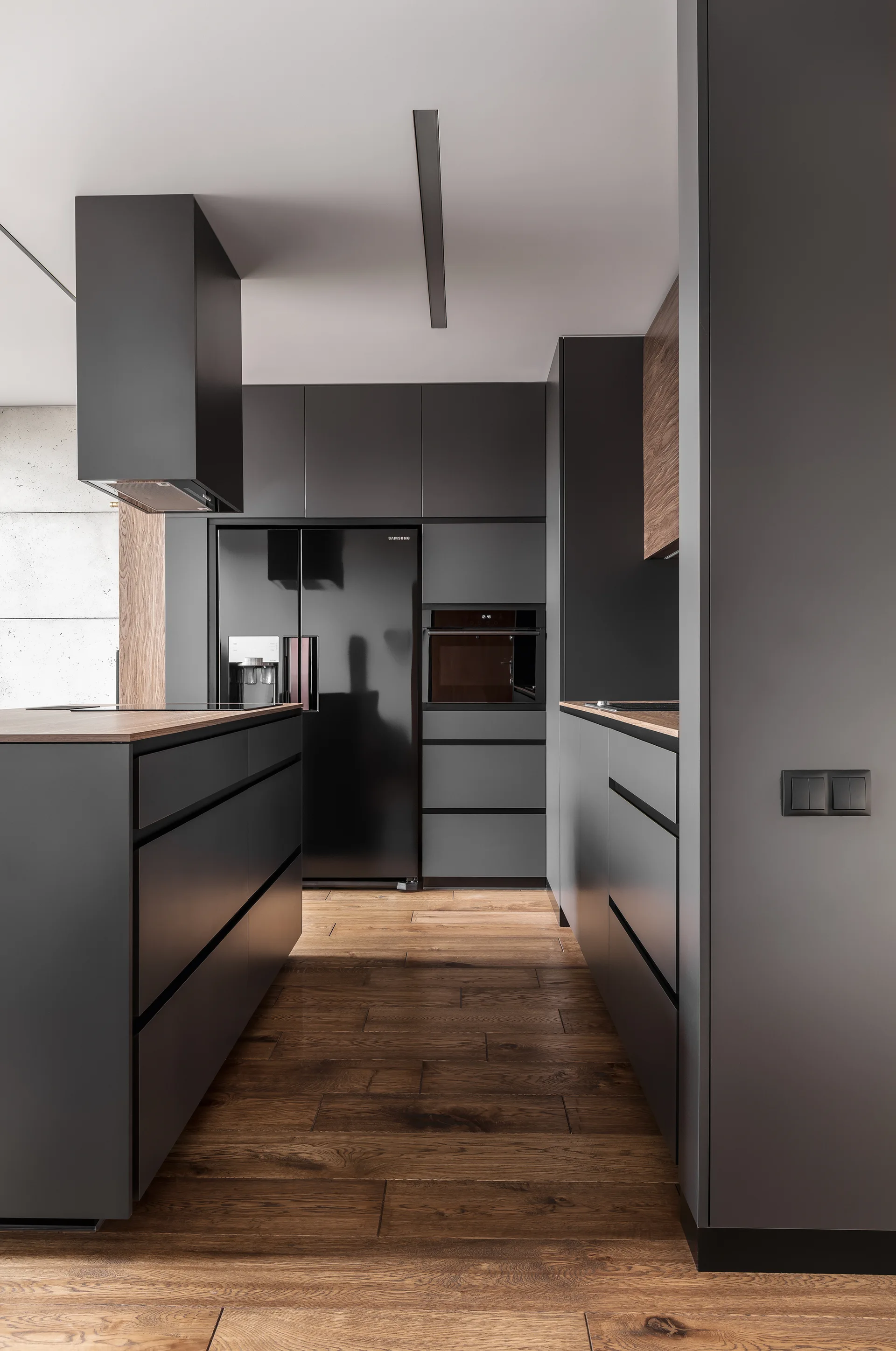 A modern kitchen featuring matte charcoal grey handleless cabinets, a central island with a wood countertop, and warm wood flooring.