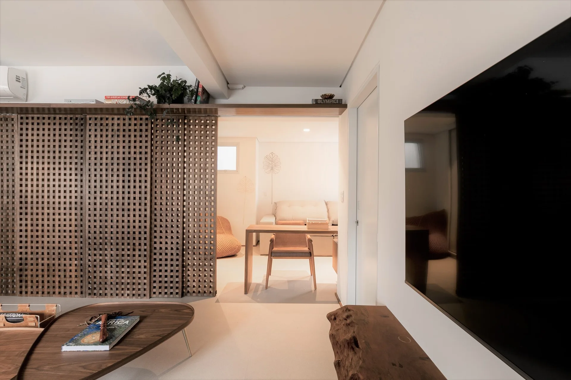 A minimalist living room features a dark wooden lattice partition screen alongside a wall-mounted TV and a low curved wood coffee table.