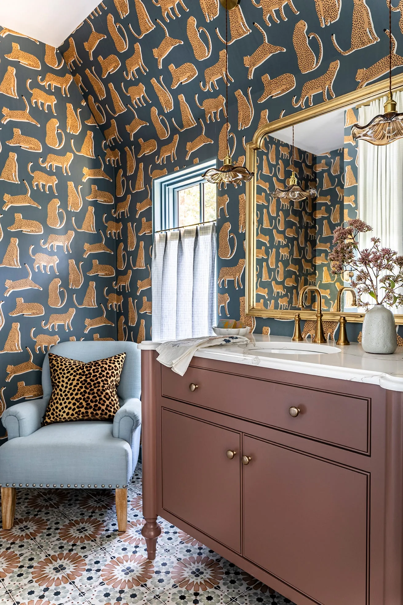 A powder room features dark leopard print wallpaper, a deep plum vanity with a marble countertop, and a light blue armchair.