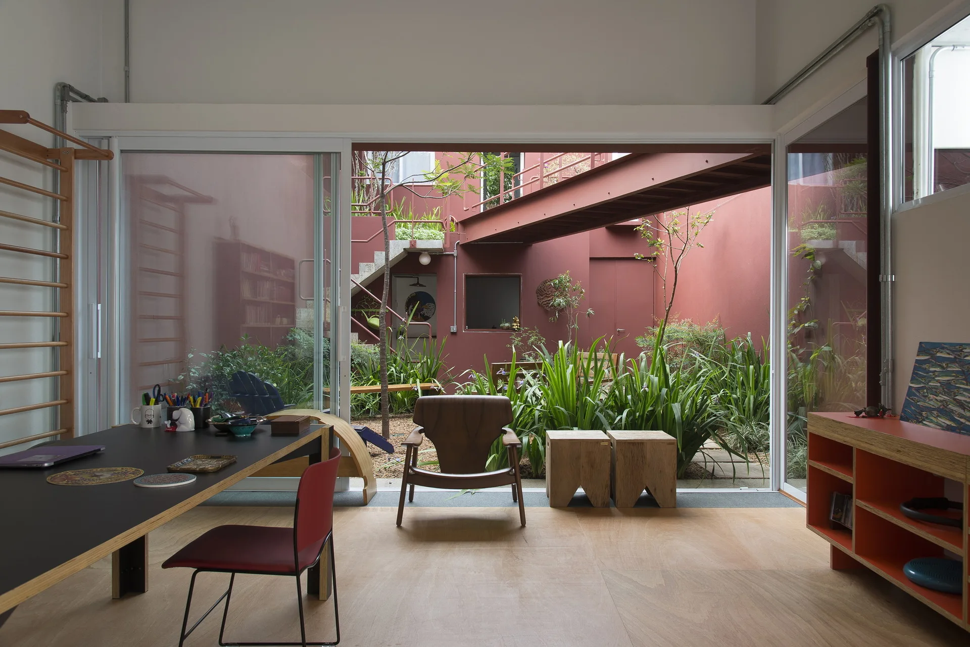 An interior room with wood floors and a desk looking out through large sliding glass doors to a reddish courtyard with plants.